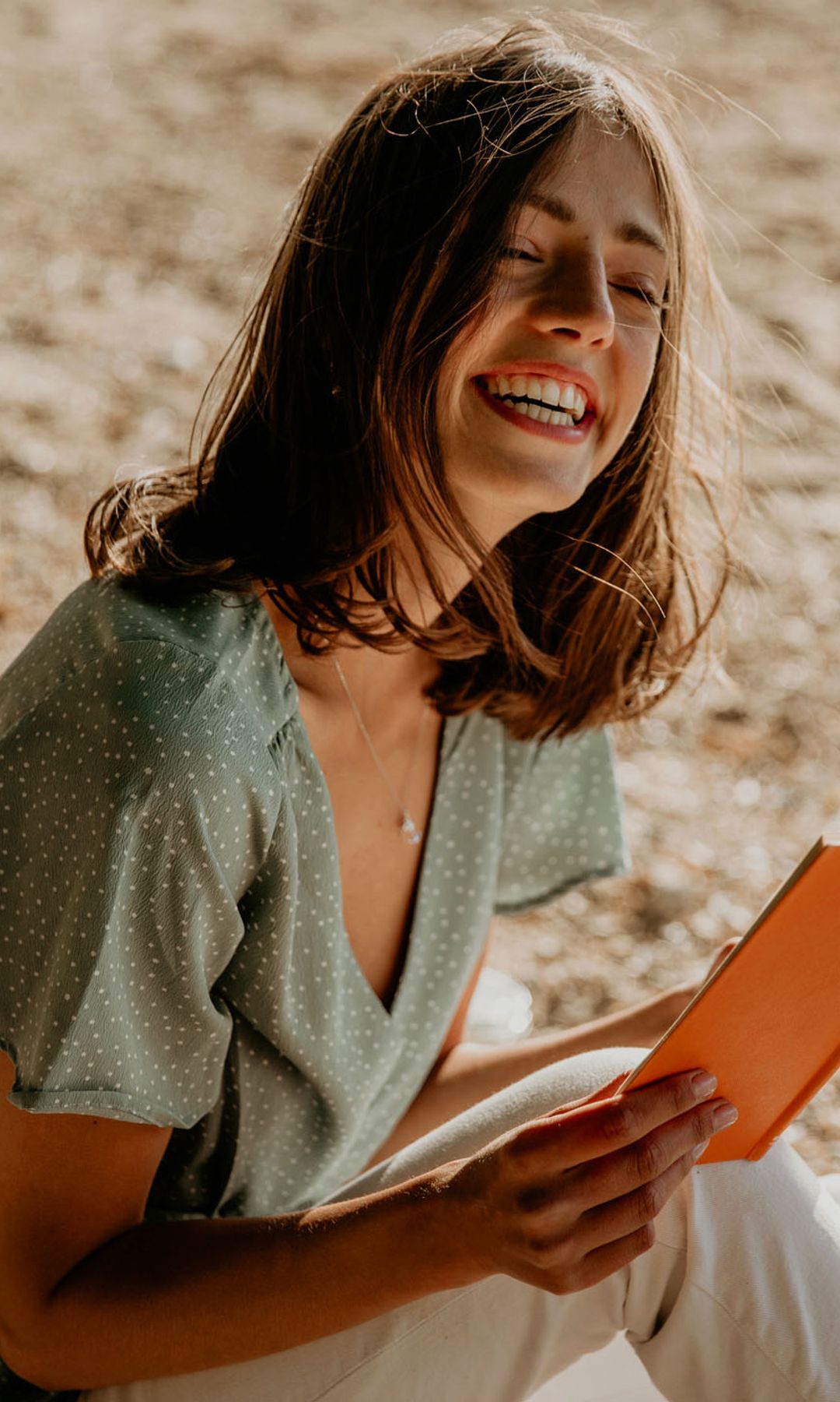 Mujer riendo leyendo un libro en la arena 