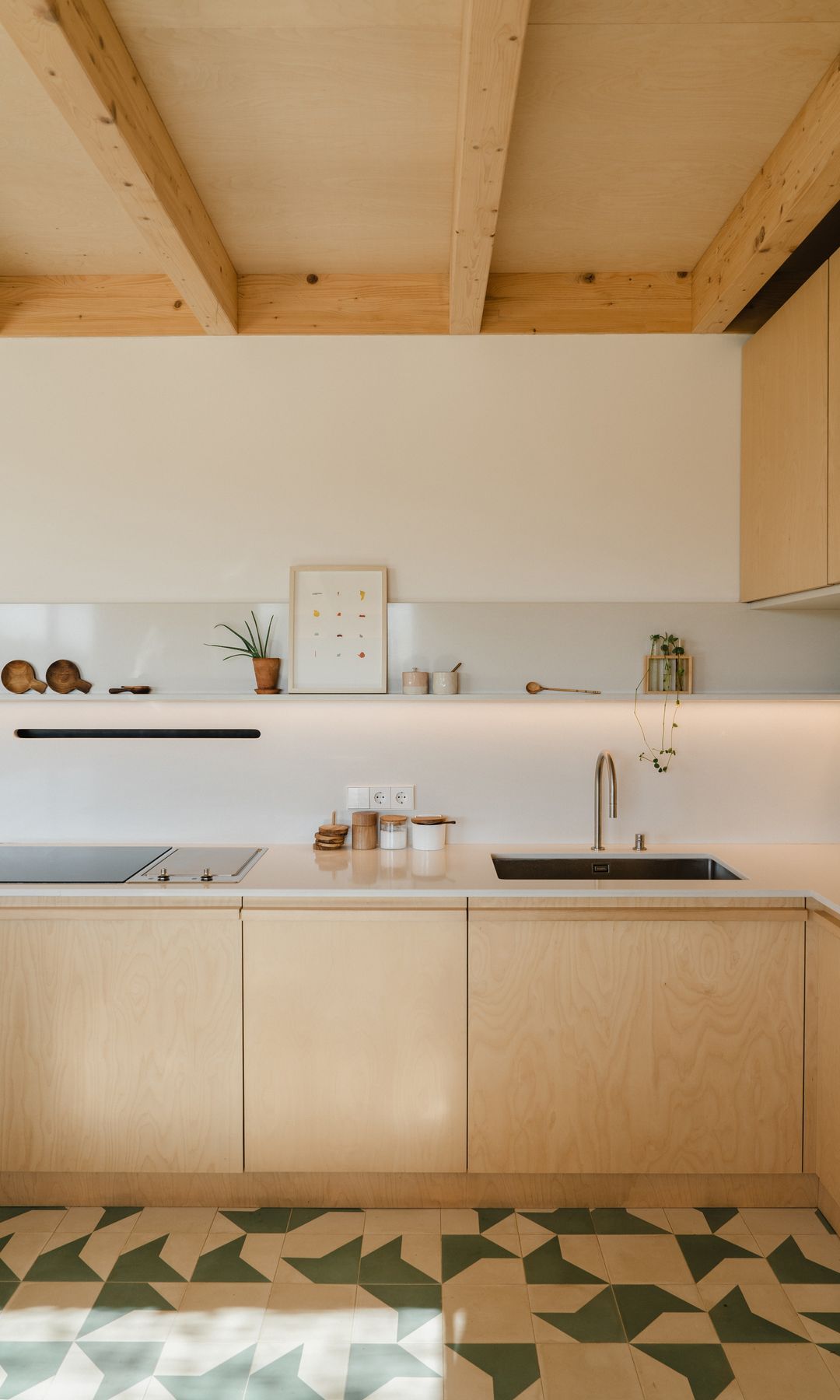 Cocina de madera, con balda en lugar de armarios superiores, alfombra de motivos geométricos, luz bajo las baldas