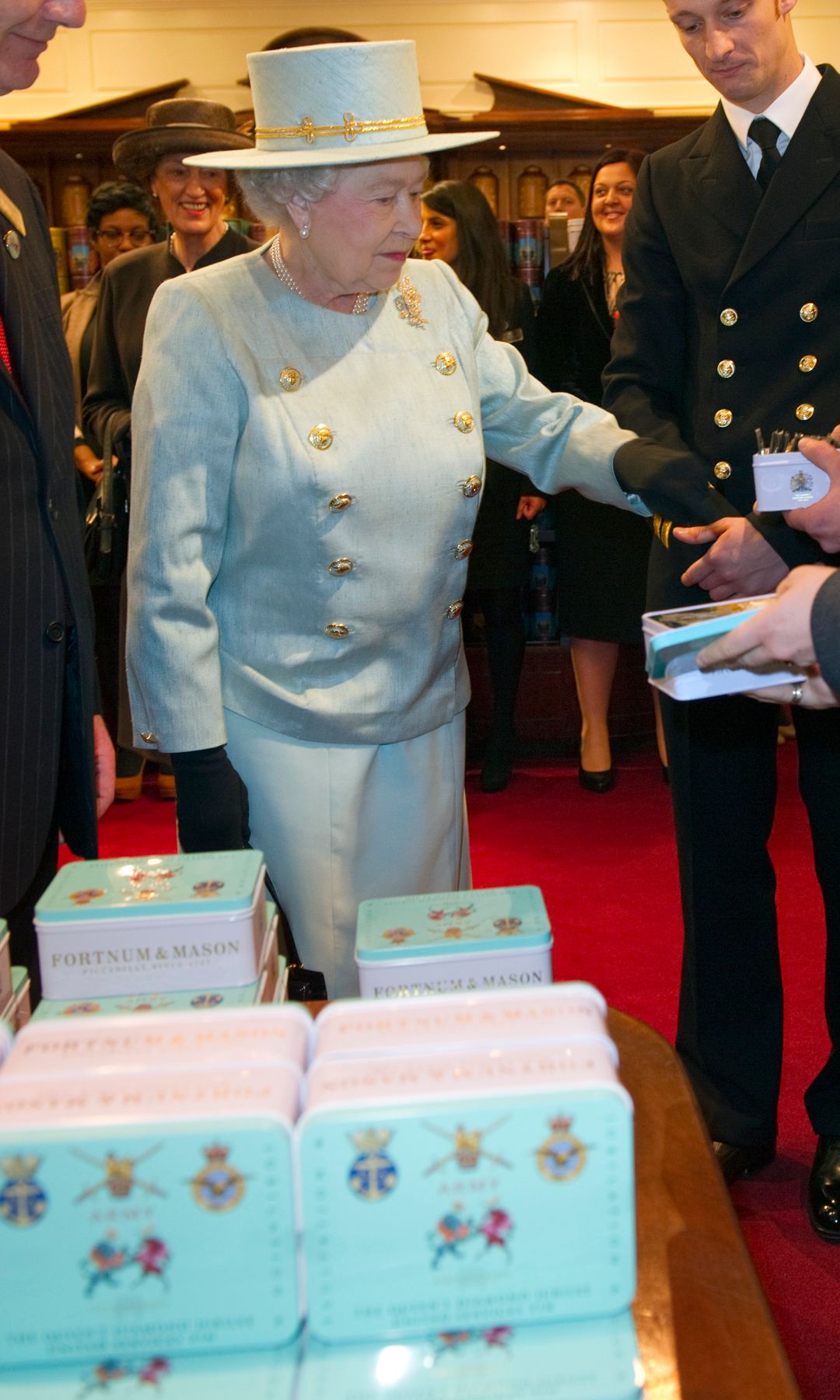 Isabel II en Fortnum & Mason de Londres ante unas cajas de galletas con los escudos de la Familia Real británica, puro merchandising al estilo británico