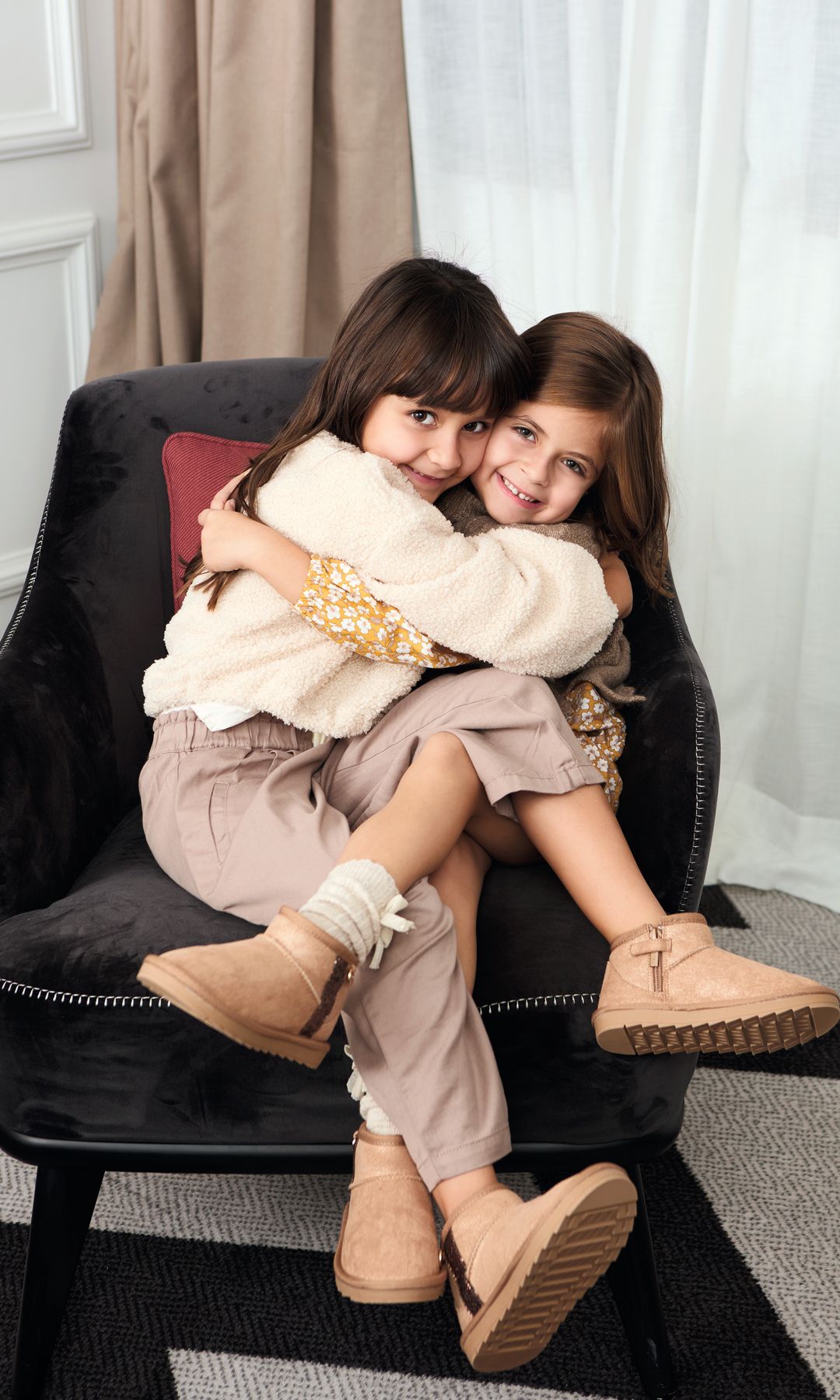 Dos niñas en una silla, abrazadas, con botas beige y ropa informal
