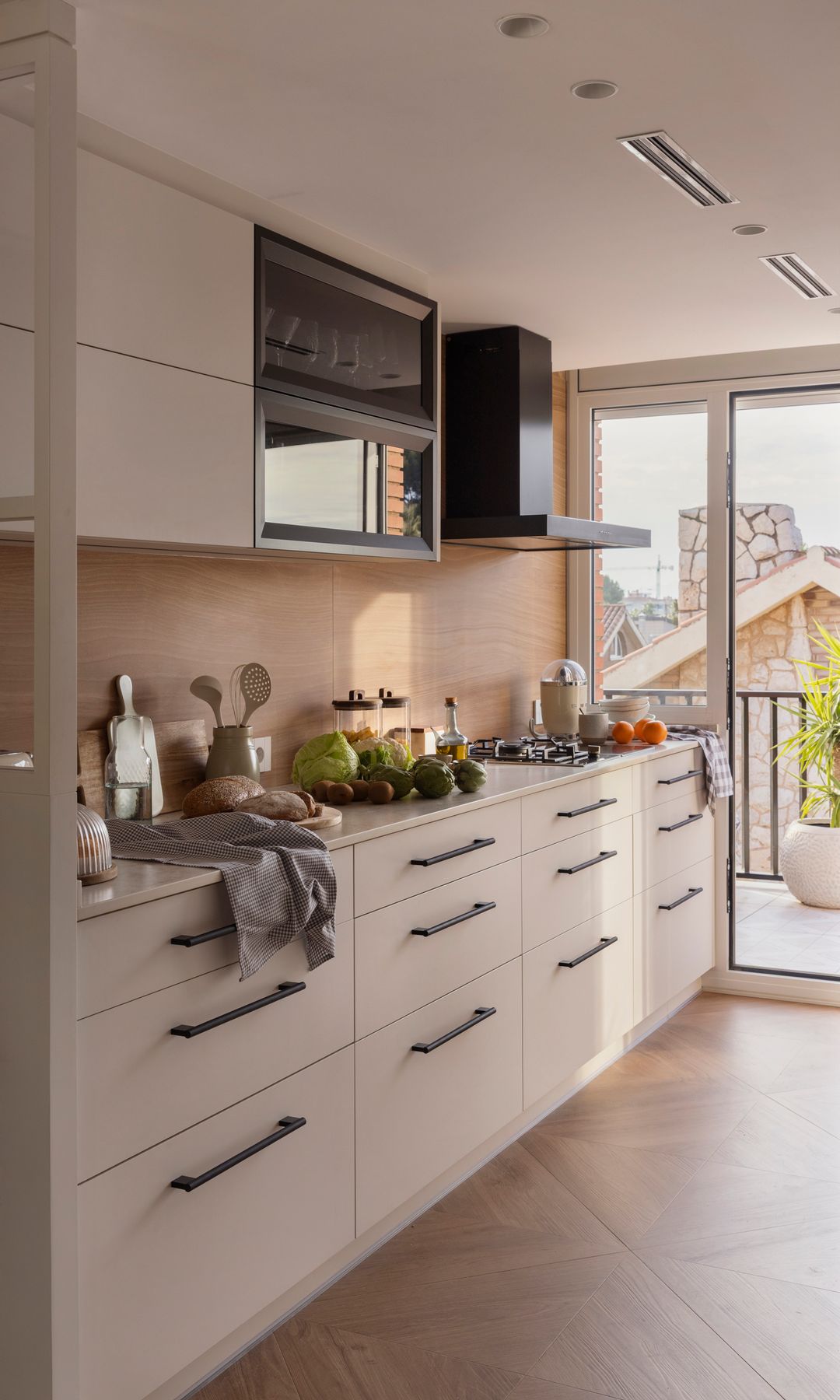 Cocina blanca con tiradores negros, suelo de madera y salida a la terraza