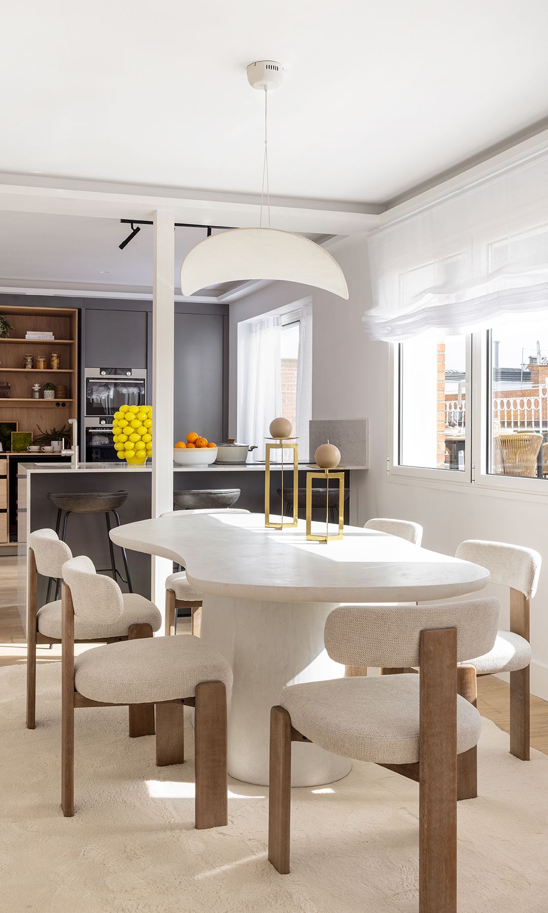 Comedor con mesa blanca de formas escultóricas, sillas tapizadas en blanco, estores blancos