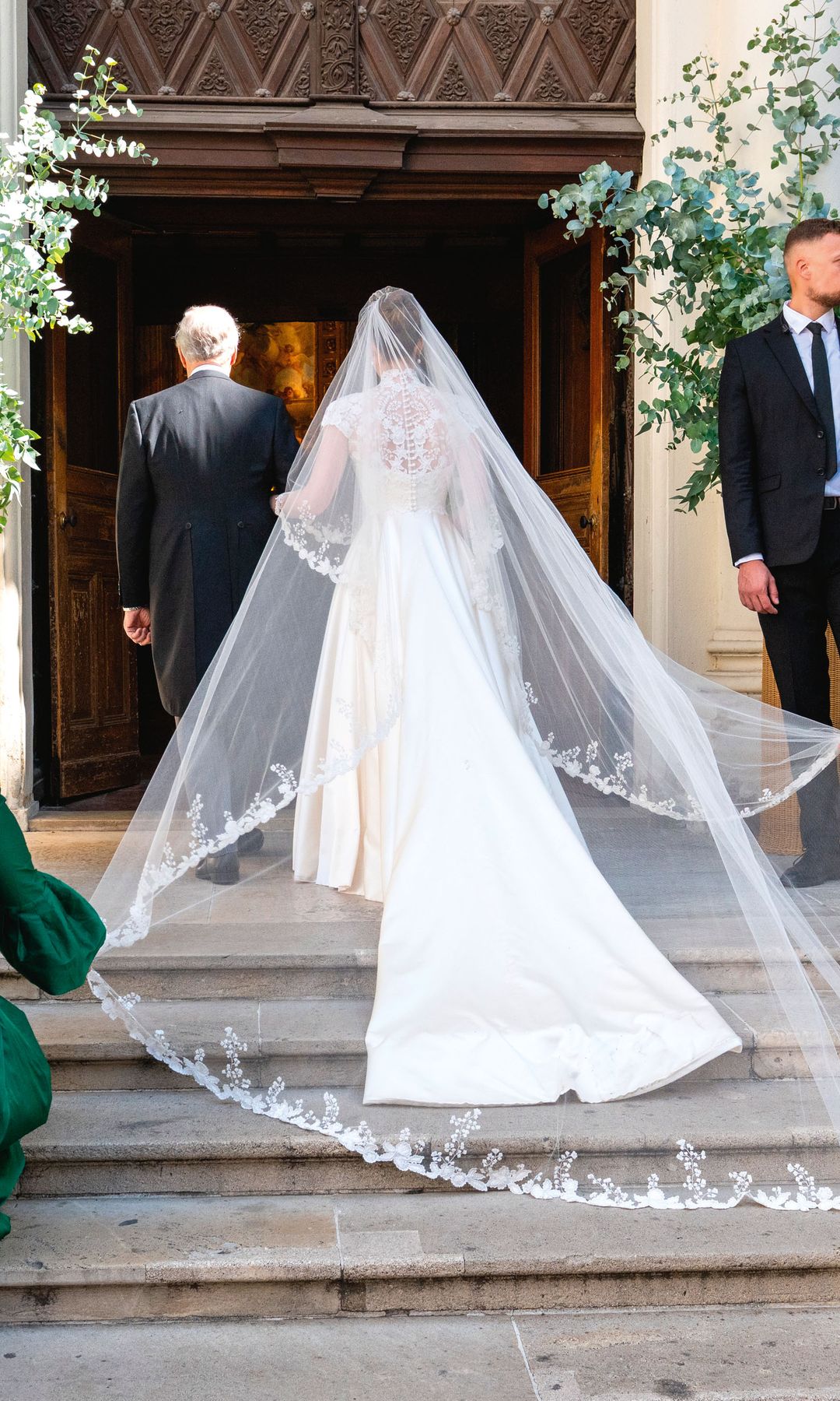 La novia entrando en la iglesia con su padre y padrino mientras la ayudan a llevar su velo