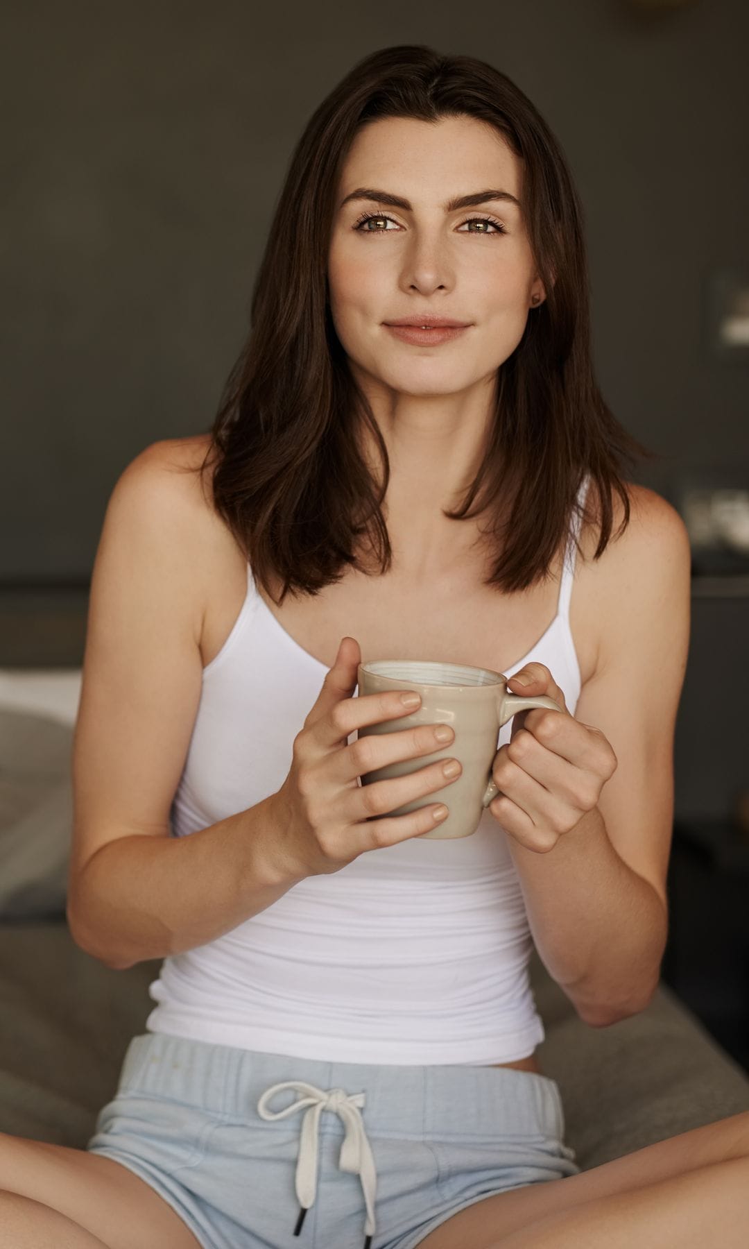 Una mujer en pijama tomando un café en la cama