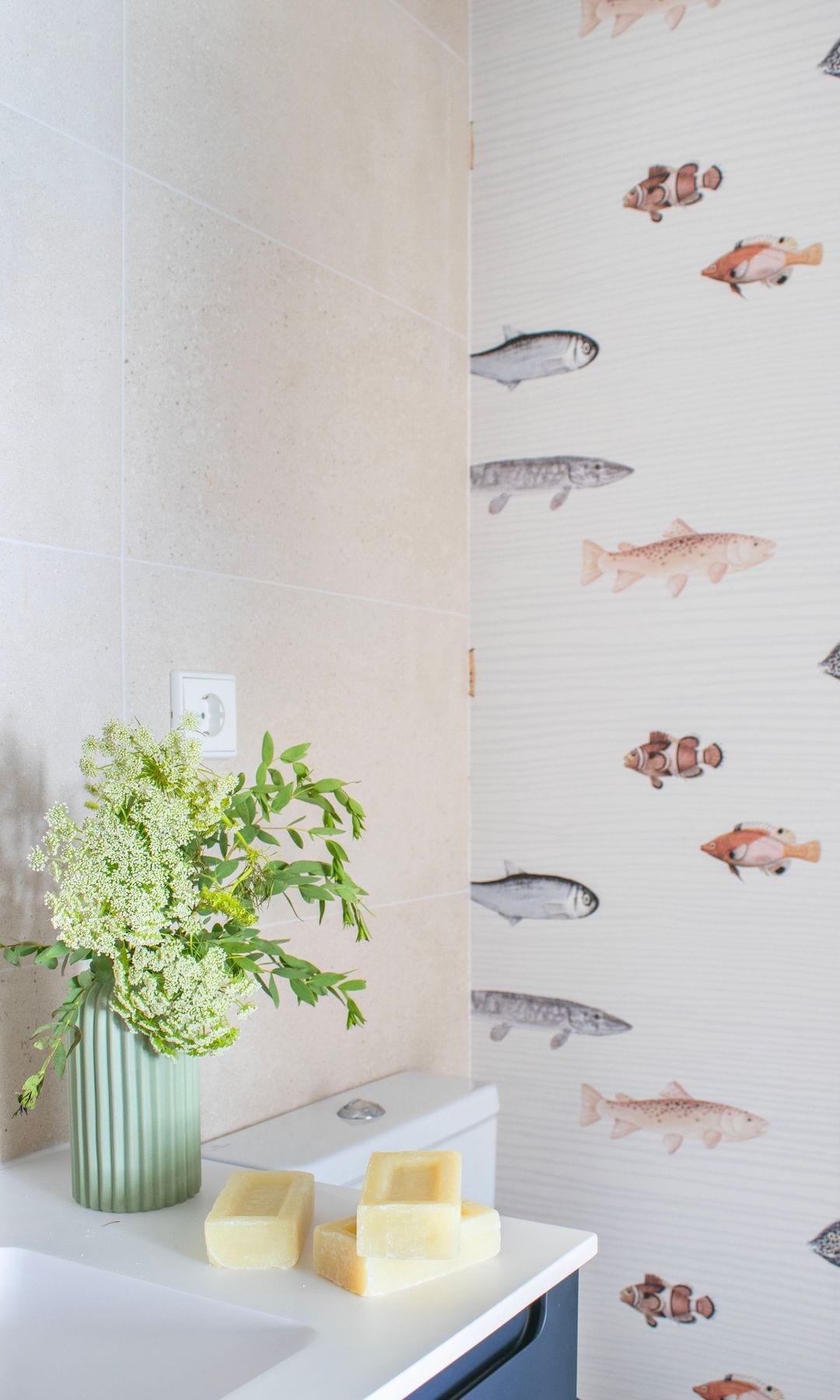 Baño con papel pintado, de peces, jarrón verde con flores, pastillas de jabón