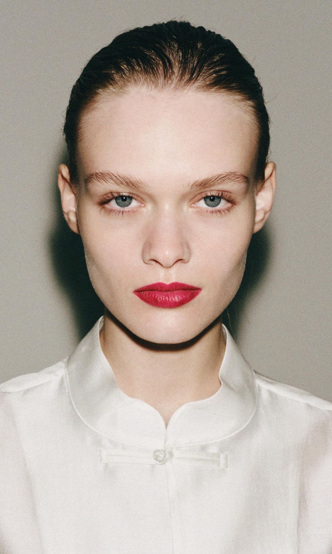 Rostro de modelo de Zara con pelo recogido, labios rojos y blusa de seda blanca