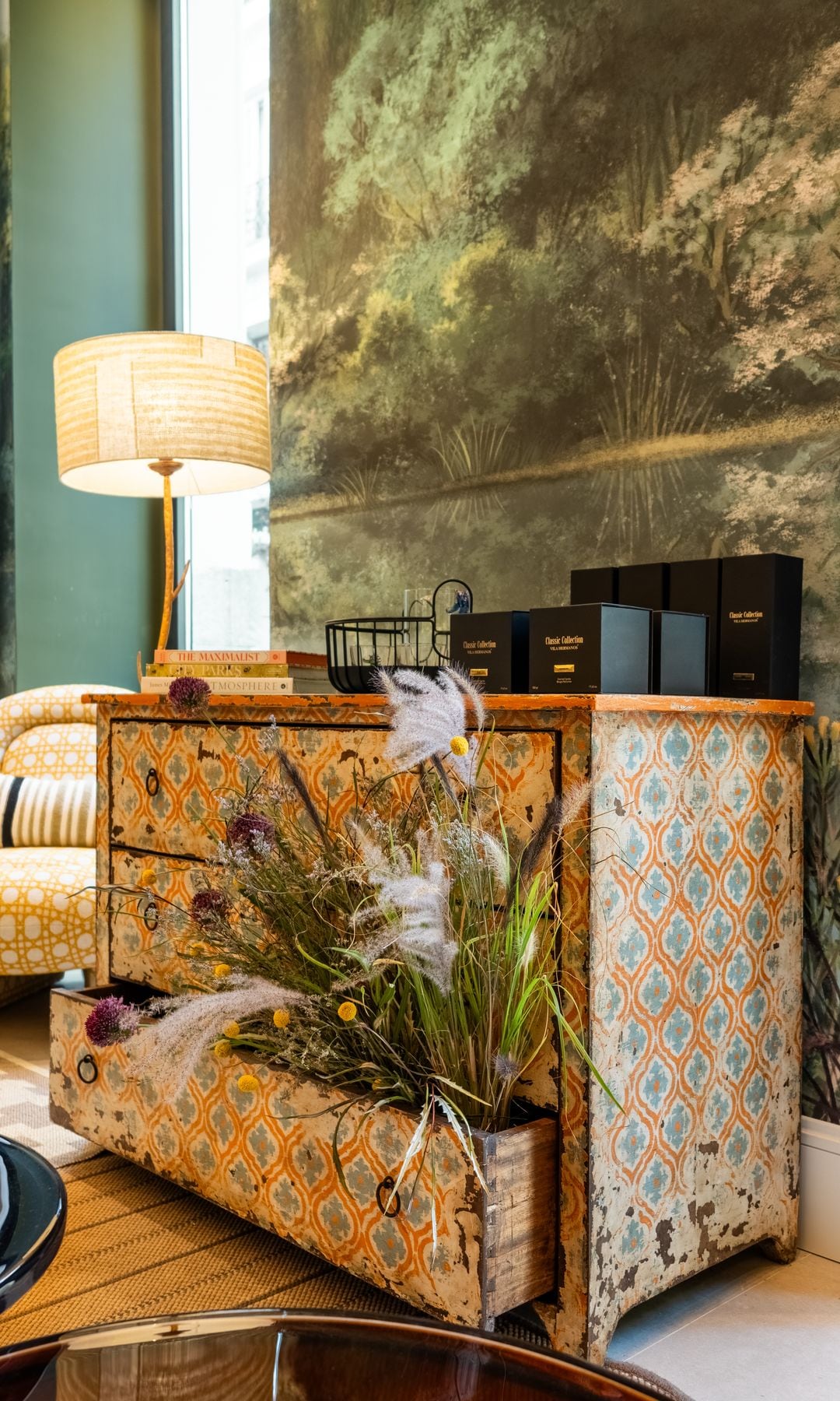 Cómoda renovada con pintura de color amarillo, lámpara de sobremesa, mural en la pared, velas y butaca