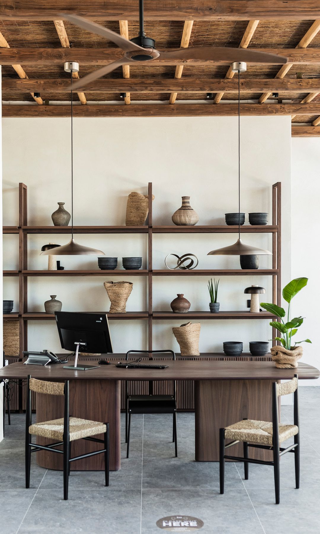 Despacho con estantería abierta de madera, mesa de madera, dos sillas, techo de madera y ventilador de techo