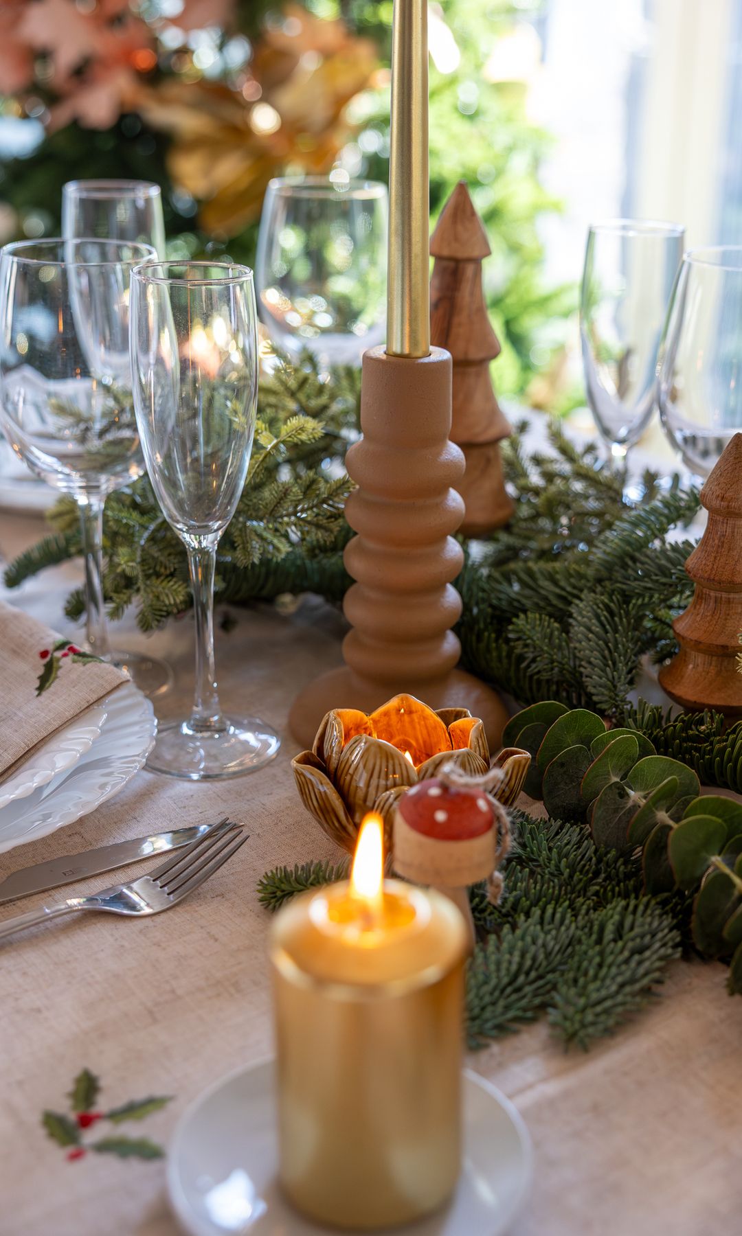 Mesa de Navidad con velas, candelabros, mantel blanco con motivos navideños, copas de cava, guirnalda verde en el centro de la mesa