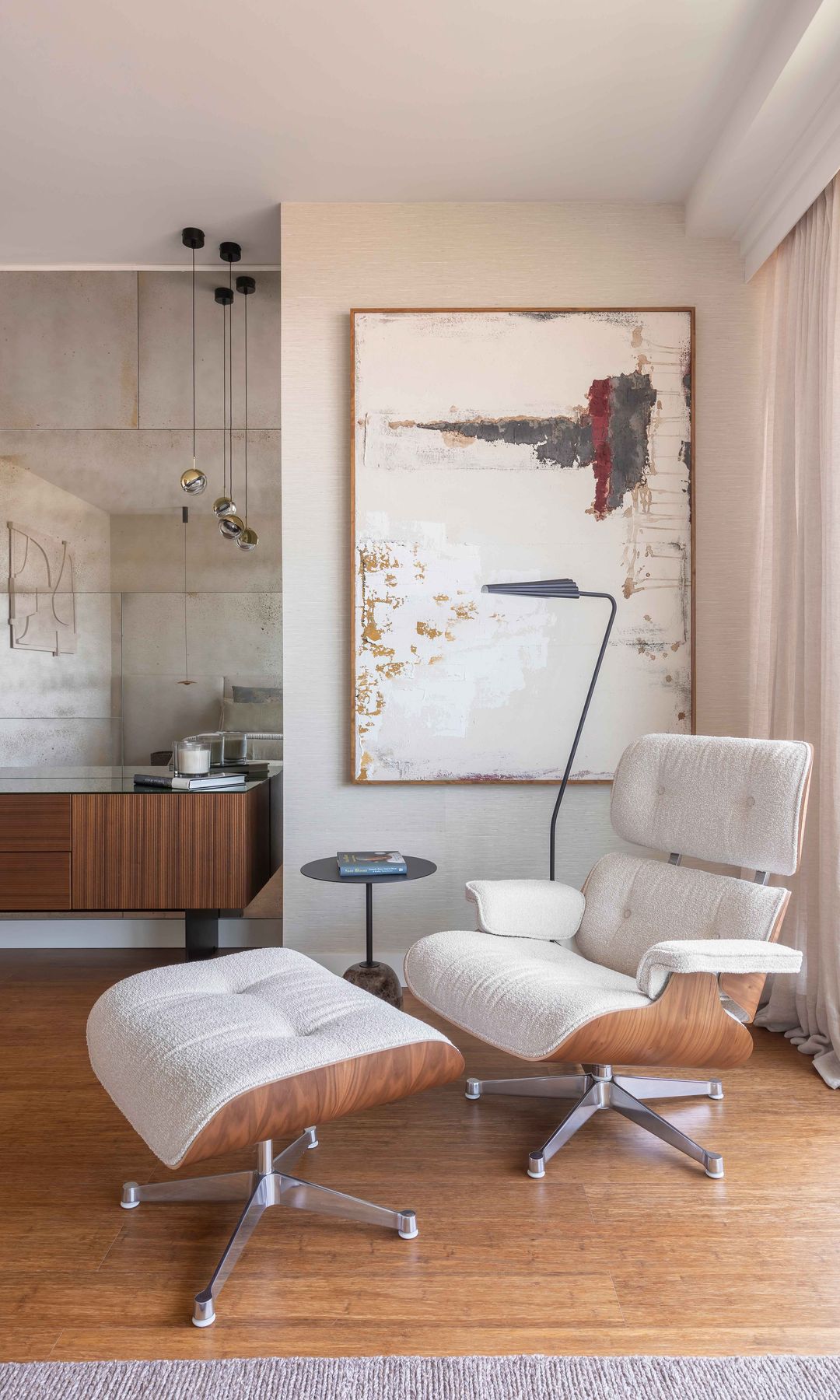 Rincón salón con chaise longue Eames de cuero blanco, cuadro en la pared, lámpara de pie, mesa auxiliar, aparador de madera oscura, suelo de madera, cortinas blancas