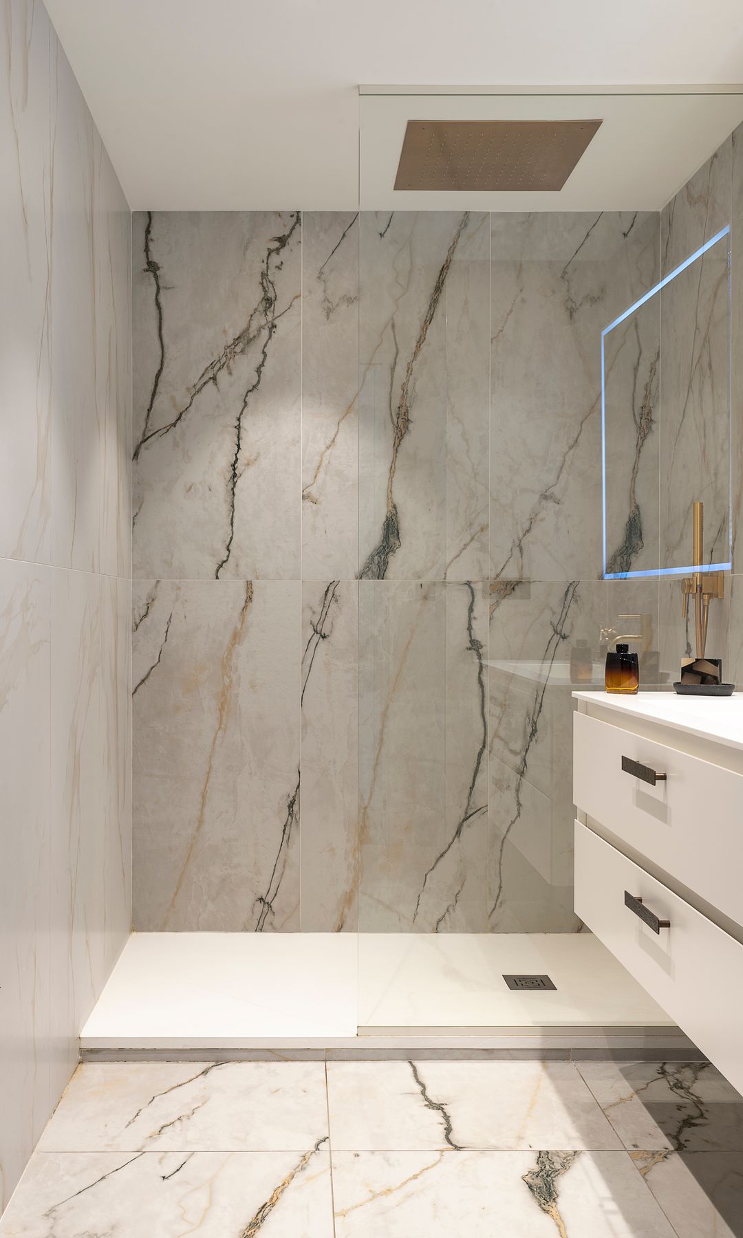 Baño con ducha, paredes y suelo porcelánicos a juego, espejo retroiluminado, radiadlo toallero, mueble bajolavabo blanco