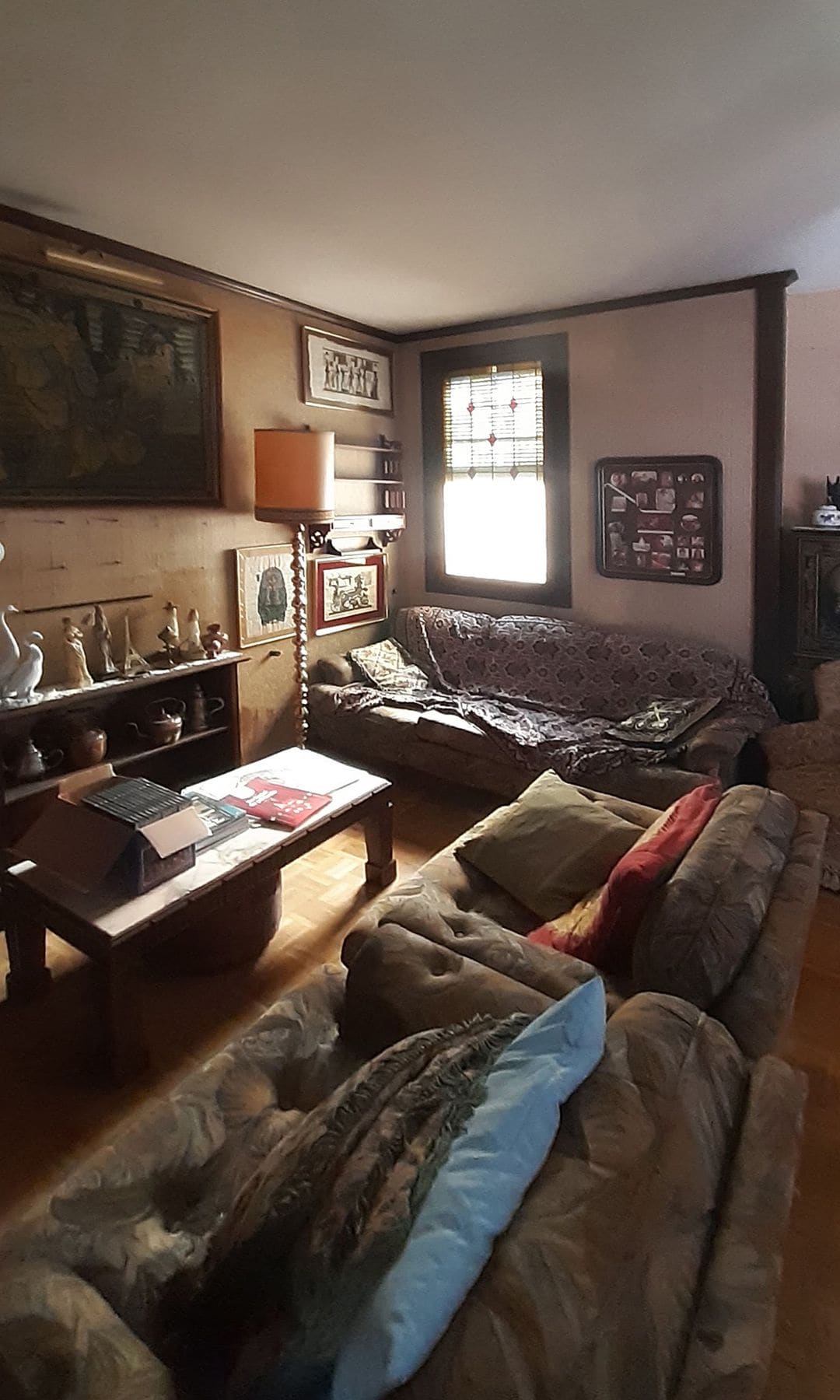 Salón antiguo, oscuro, con muebles oscuros, sofás con fundas, adornos, mesa de centro