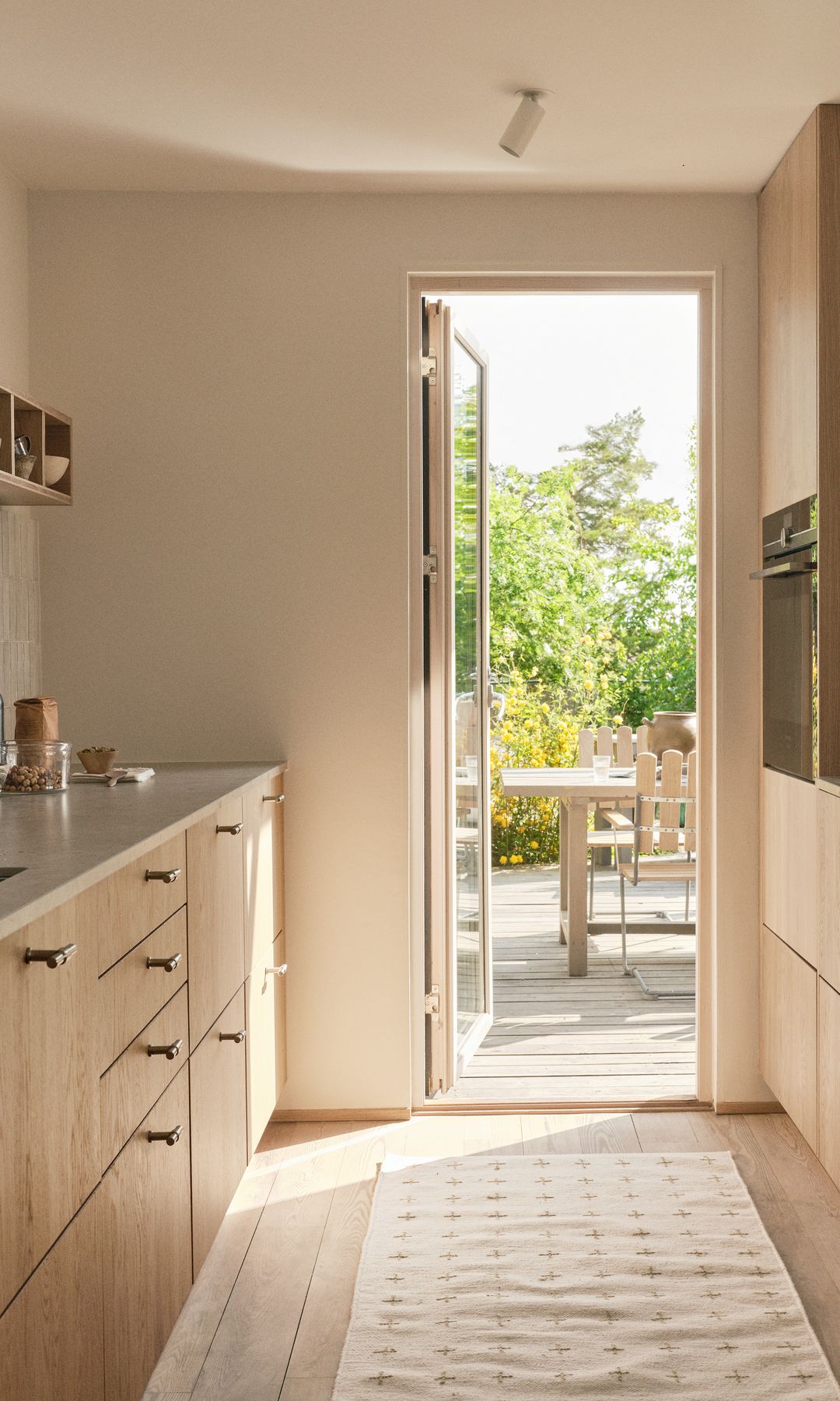 Cocina de madera clara con salida al jardín, alfombra, baldas
