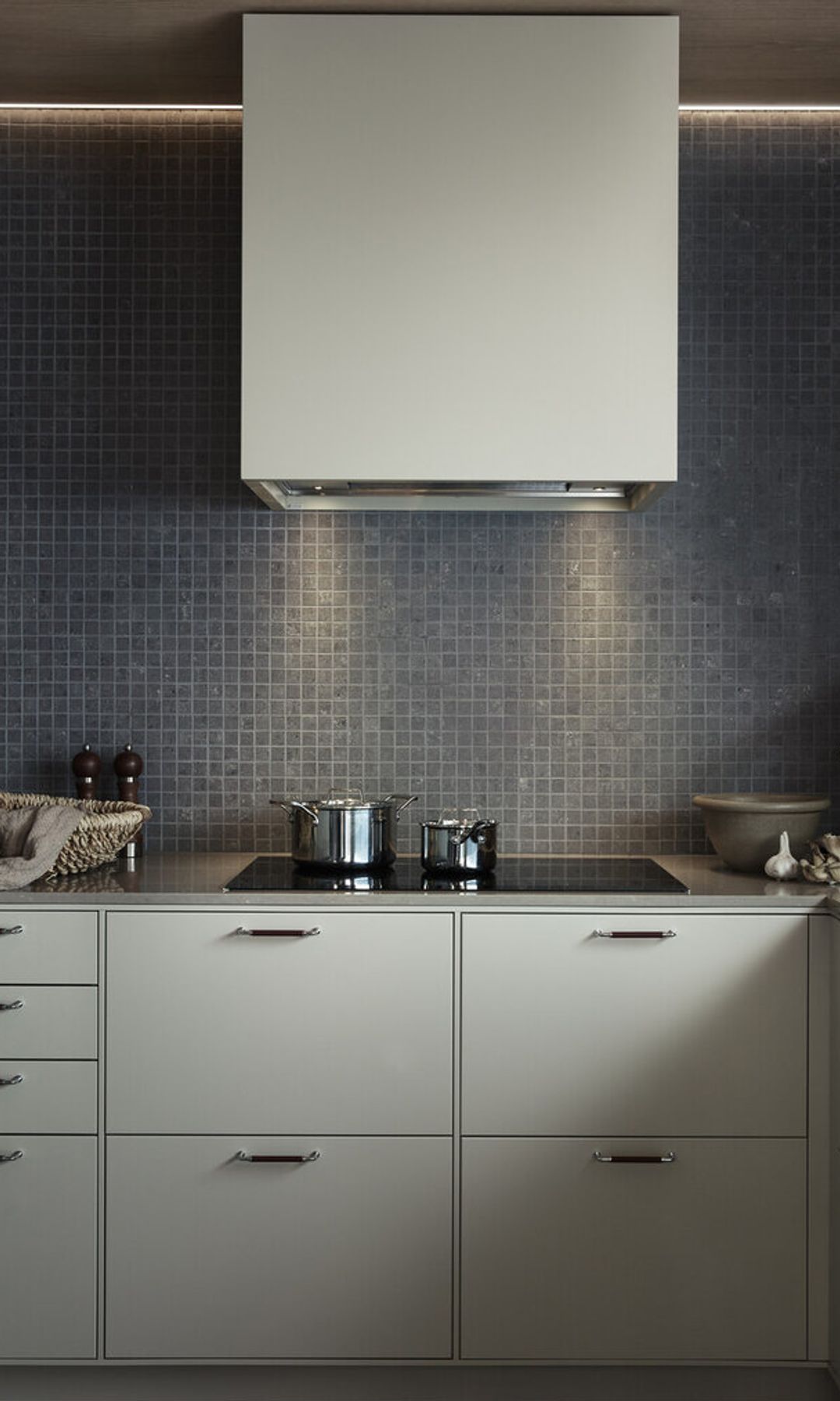 Cocina con paredes de gresite gris, campana, placa con cazuelas, muebles blancos 