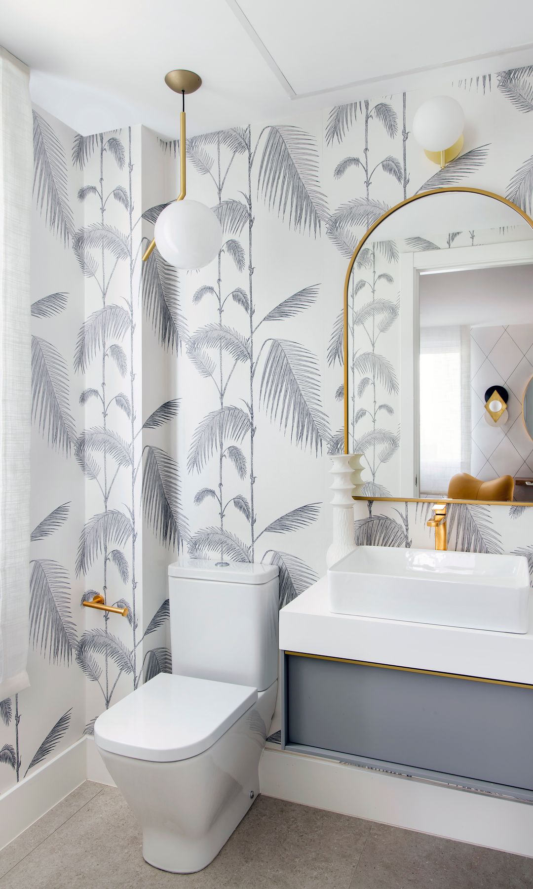 Baño con papel pintado gris a juego con el muebles, espejo dorado, lámpara de techo dorada
