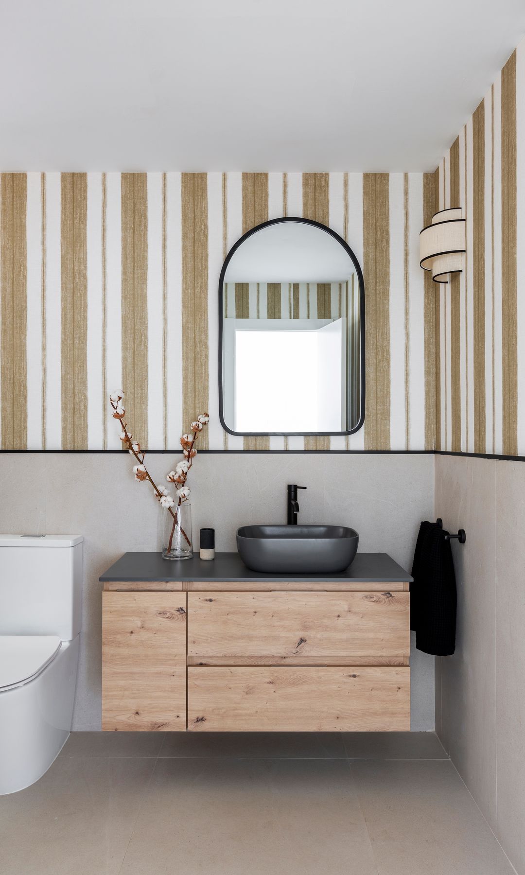 Baño con papel pintado de ratas marrones y blancas, mueble de madera y espejo ovalado con el marco negro