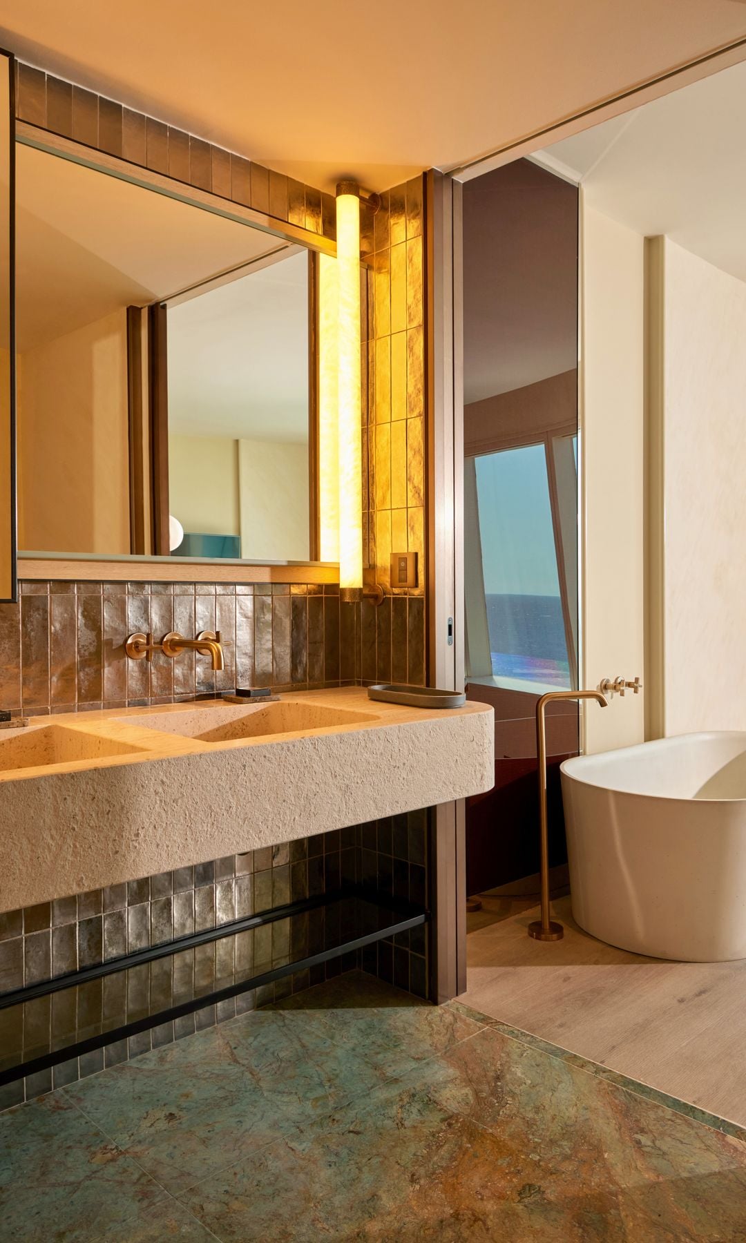 Baño con bañera exenta, espejo, encimera con lavabo integrado, pared de azulejo, suelo de madera en la bañera y de mármol en la zona de lavabo