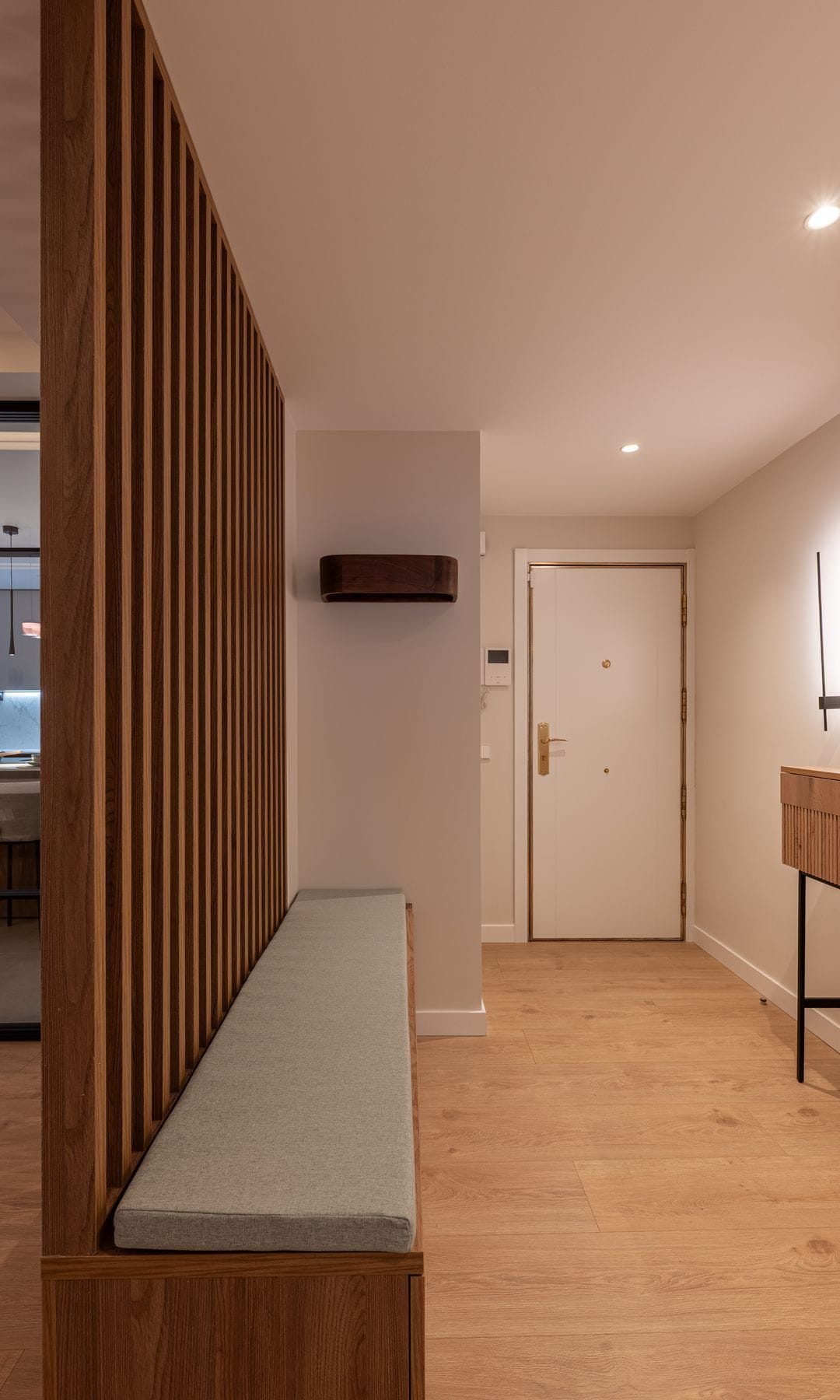 Recibidor abierto al salón con una estructura de lamas de madera verticales con banco incorporado, consola, suelo de madera