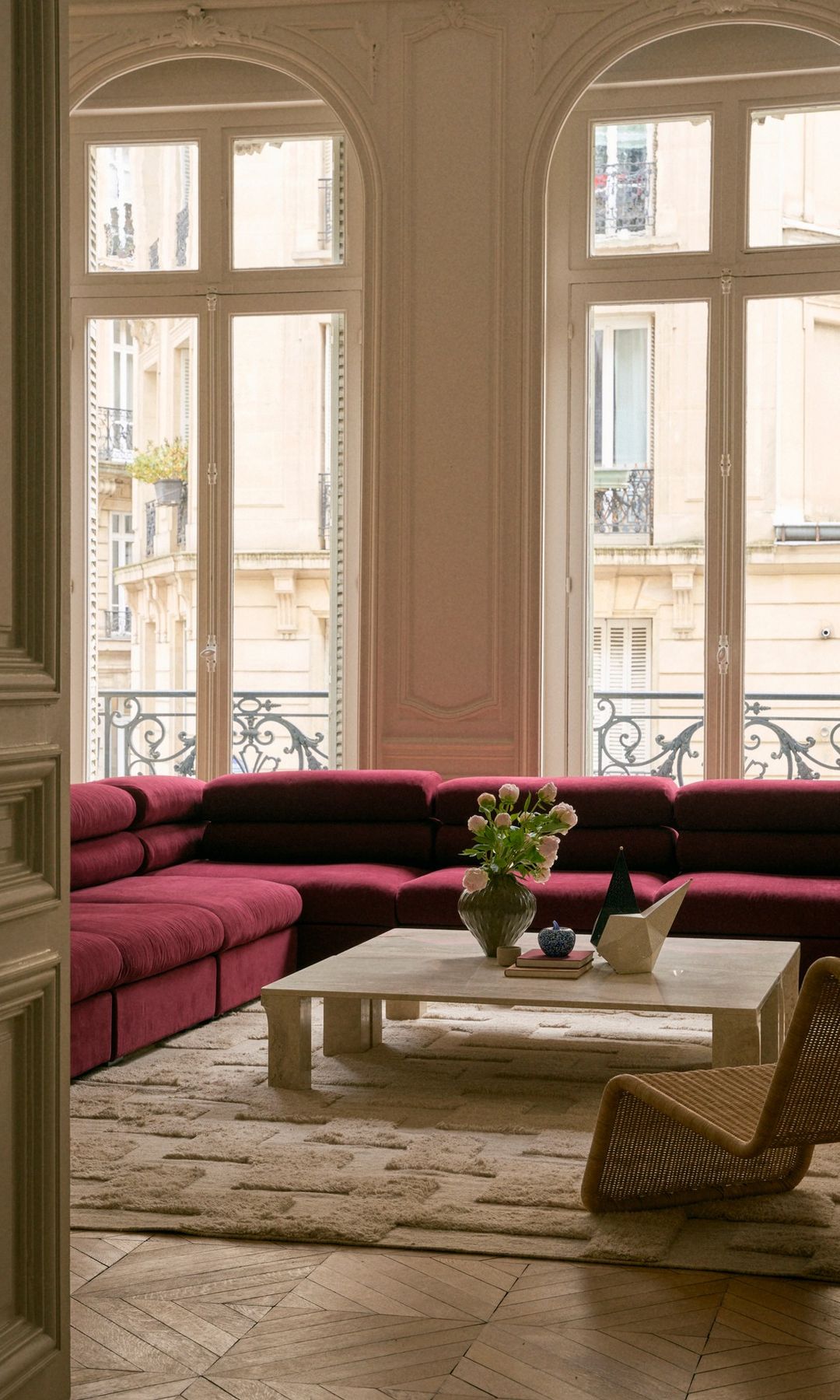 Salón con ventanales en arco blanco, sofá rojo oscuro, mesa de centro blanca, jarrón con flores, alfombra 