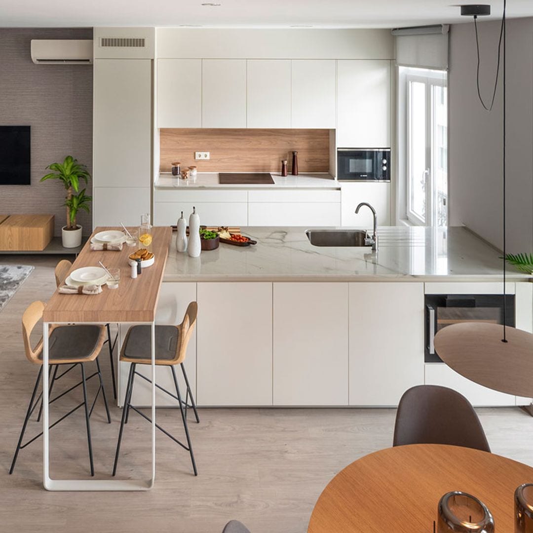 Una cocina abierta, con muebles en blanco y barra de desayunos