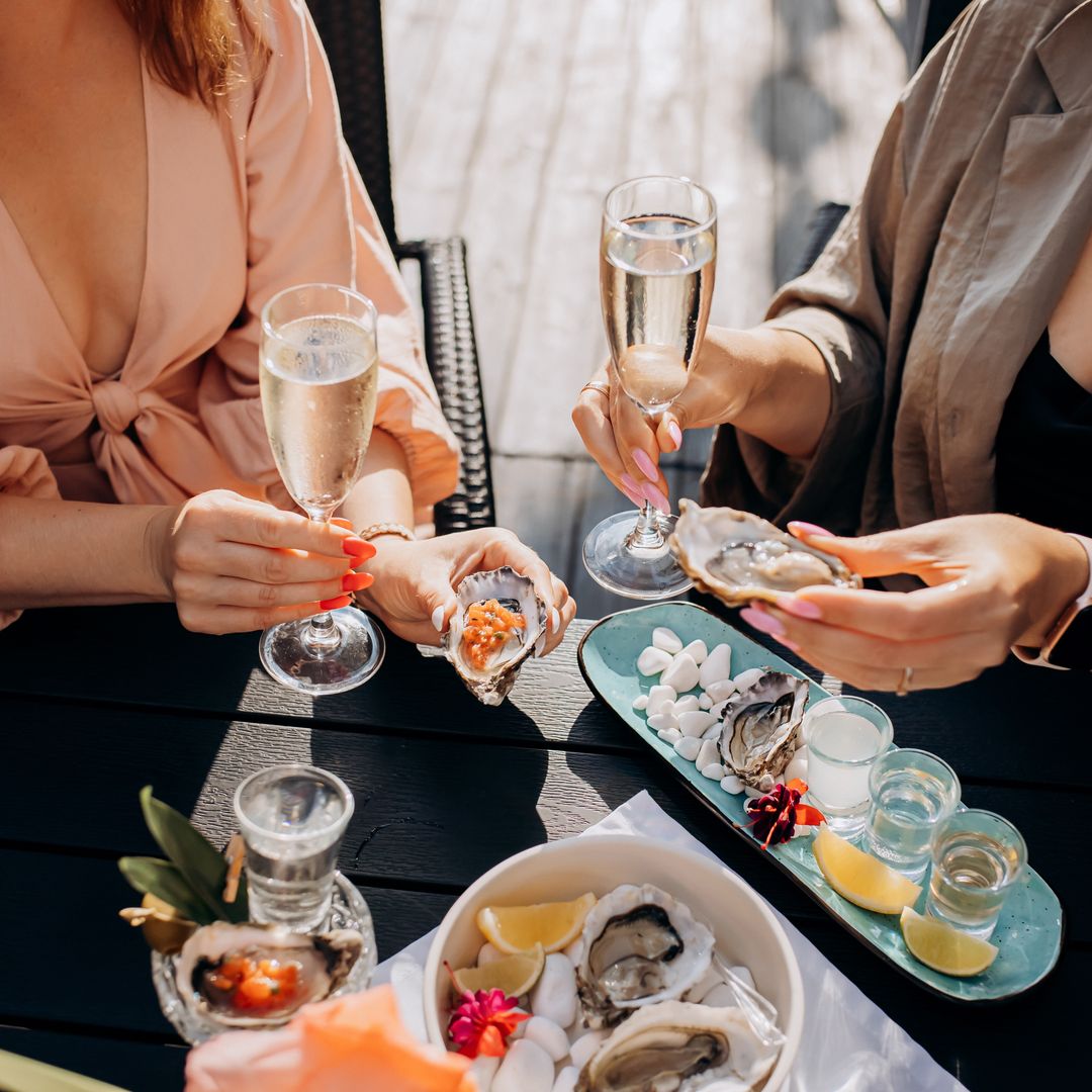 Dos mujeres brindando con champán y comiendo ostras.
