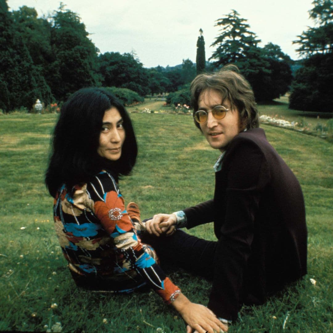 John Lennon y Yoko Ono sentados en el césped, tomados de las manos.