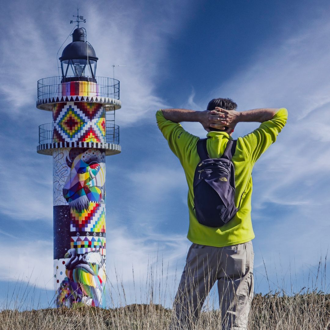 senderista aproximándose al faro pintado por okuda, cabo de ajo, Cantabria 