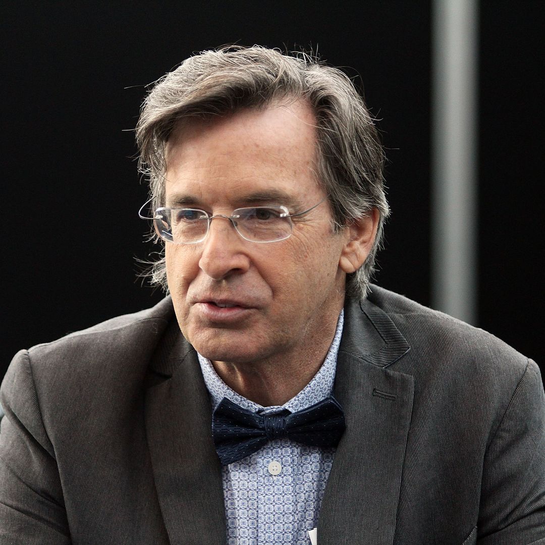 Robert Carradine en traje gris, camisa azul y pajarita 