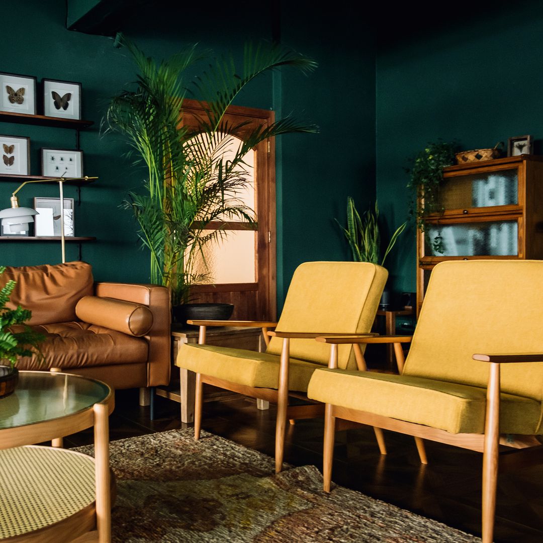 Salón decorado en amarillo mostaza y verde, con sofá de cuero y plantas.