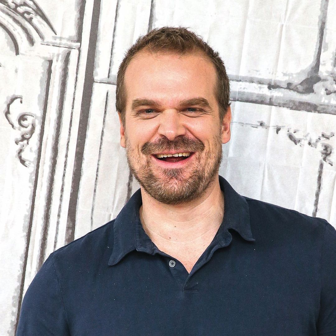 David Harbour sonriendo, con polo azul y jeans