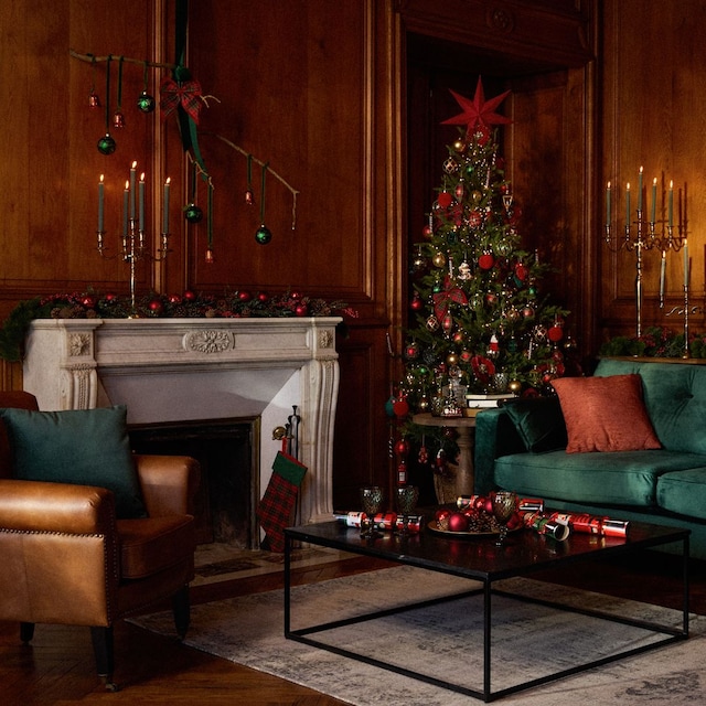 Salón con sofá verde oscuro de terciopelo, chimenea con árbol de Navidad y decoración navideña