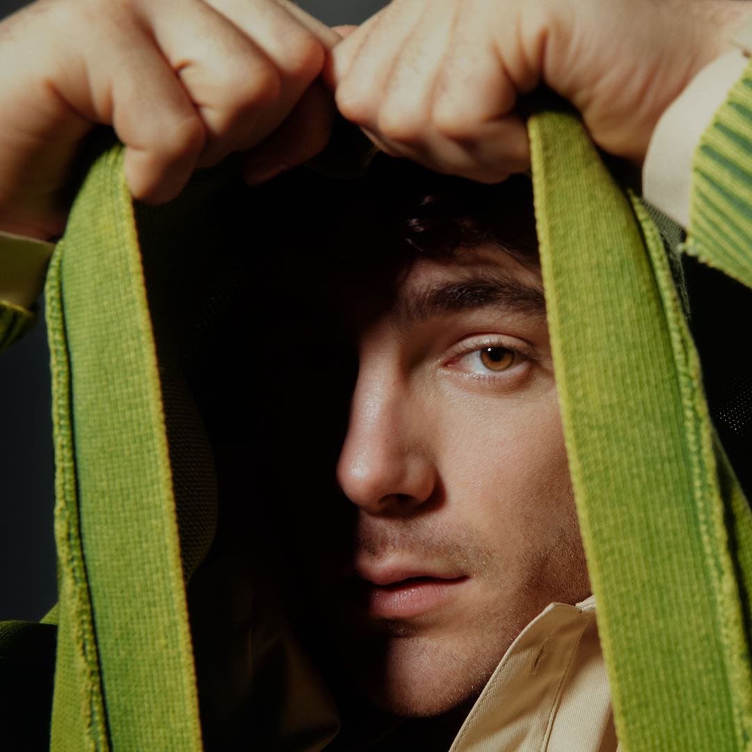 Ters con suéter verde y capucha, ocultando parcialmente su rostro.