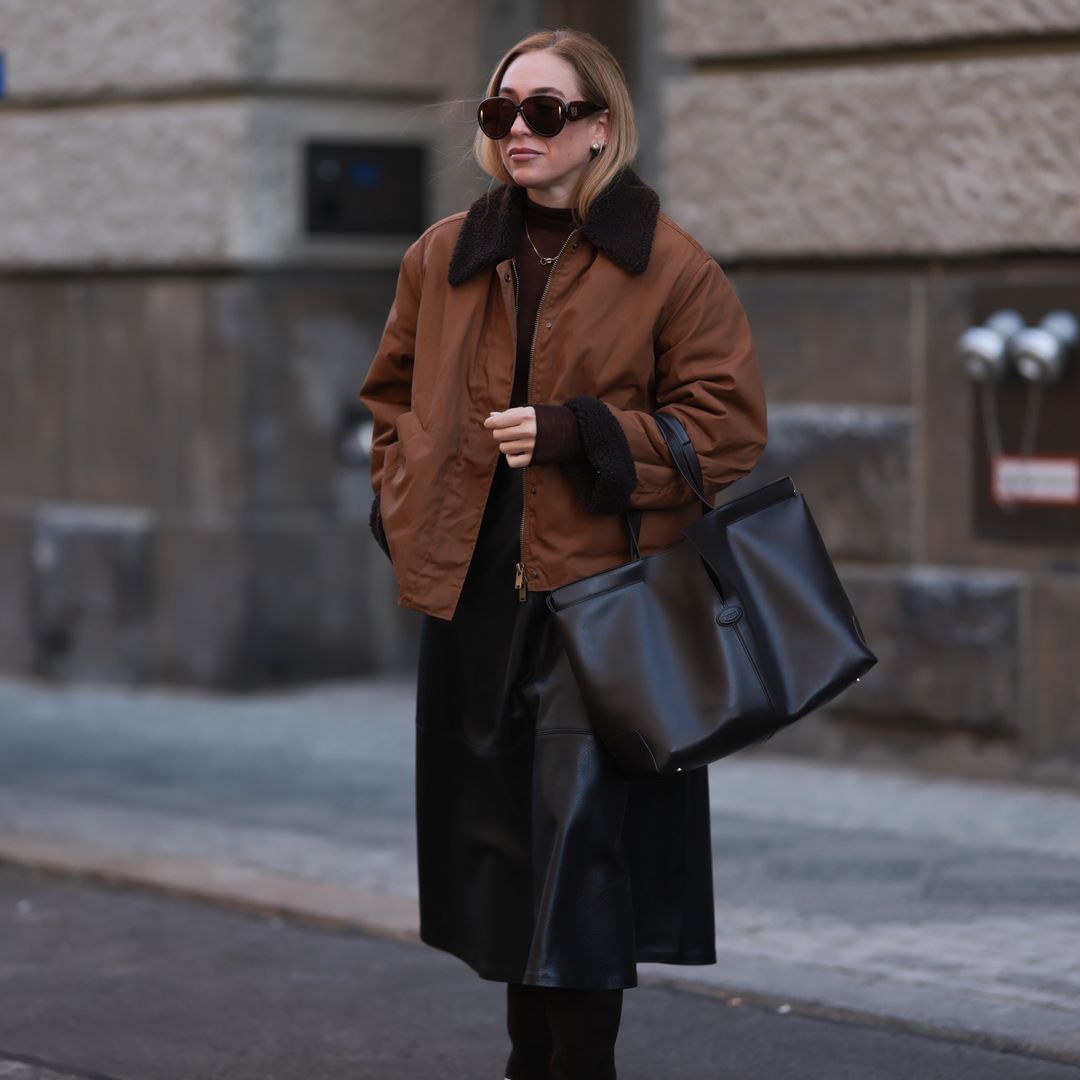 Look con bolso tote negro de piel, abrigo marrón y falda midi de cuero