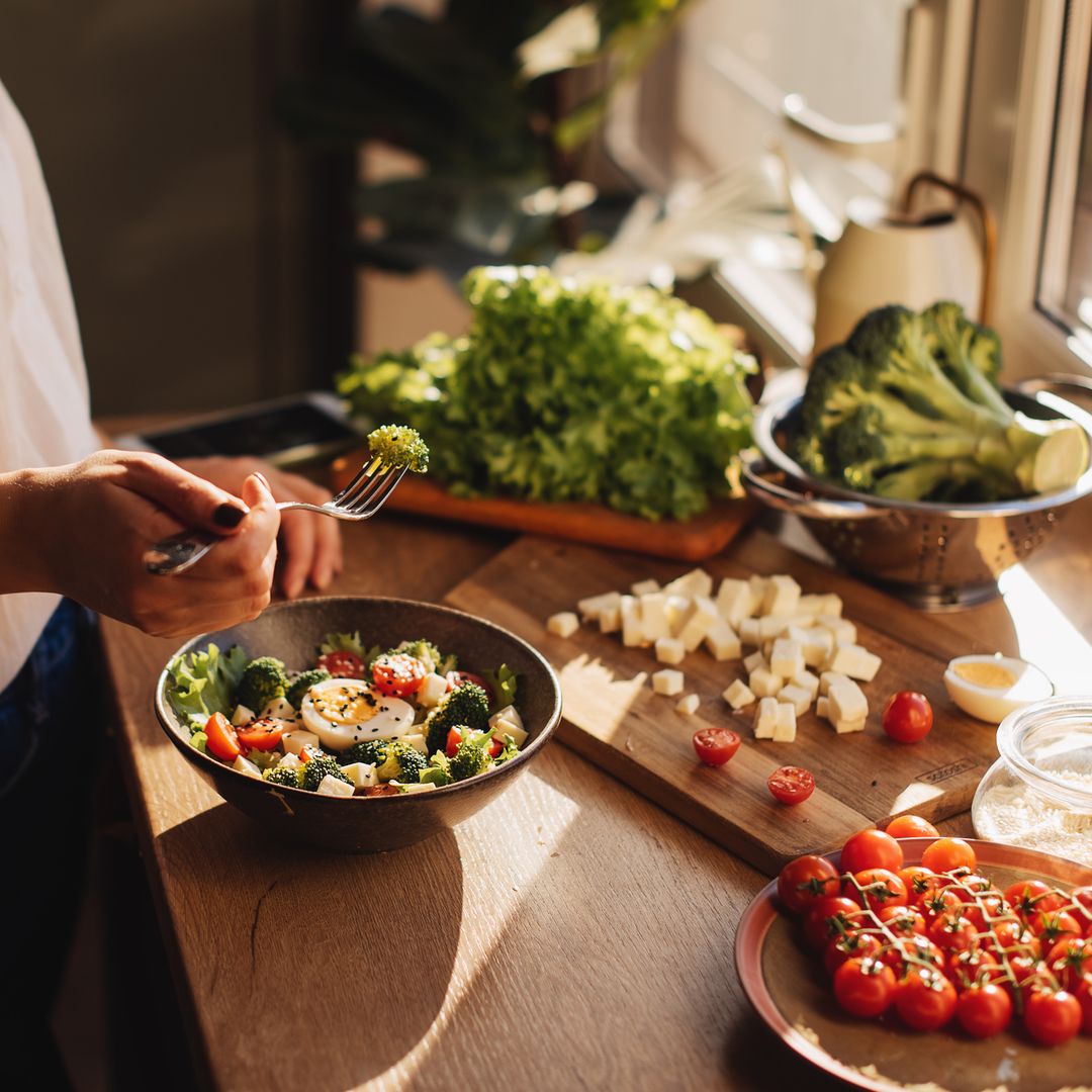 Healthy dinner or lunch. Woman in t-shirt and jeans standing and holding vegan superbowl or Buddha bowl with hummus, vegetable, salad, beans, couscous and avocado and smoothie in hands, square crop