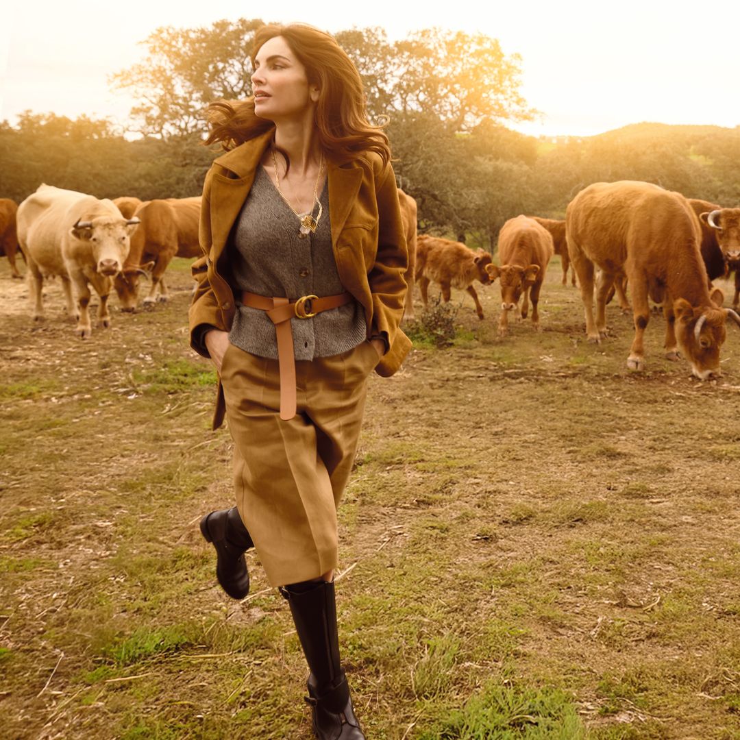 Eugenia Silva caminando en un campo con vacas al atardecer, al celebrar con "¡HOLA!" sus fabulosos 50 años en su casa de campo de Extremadura