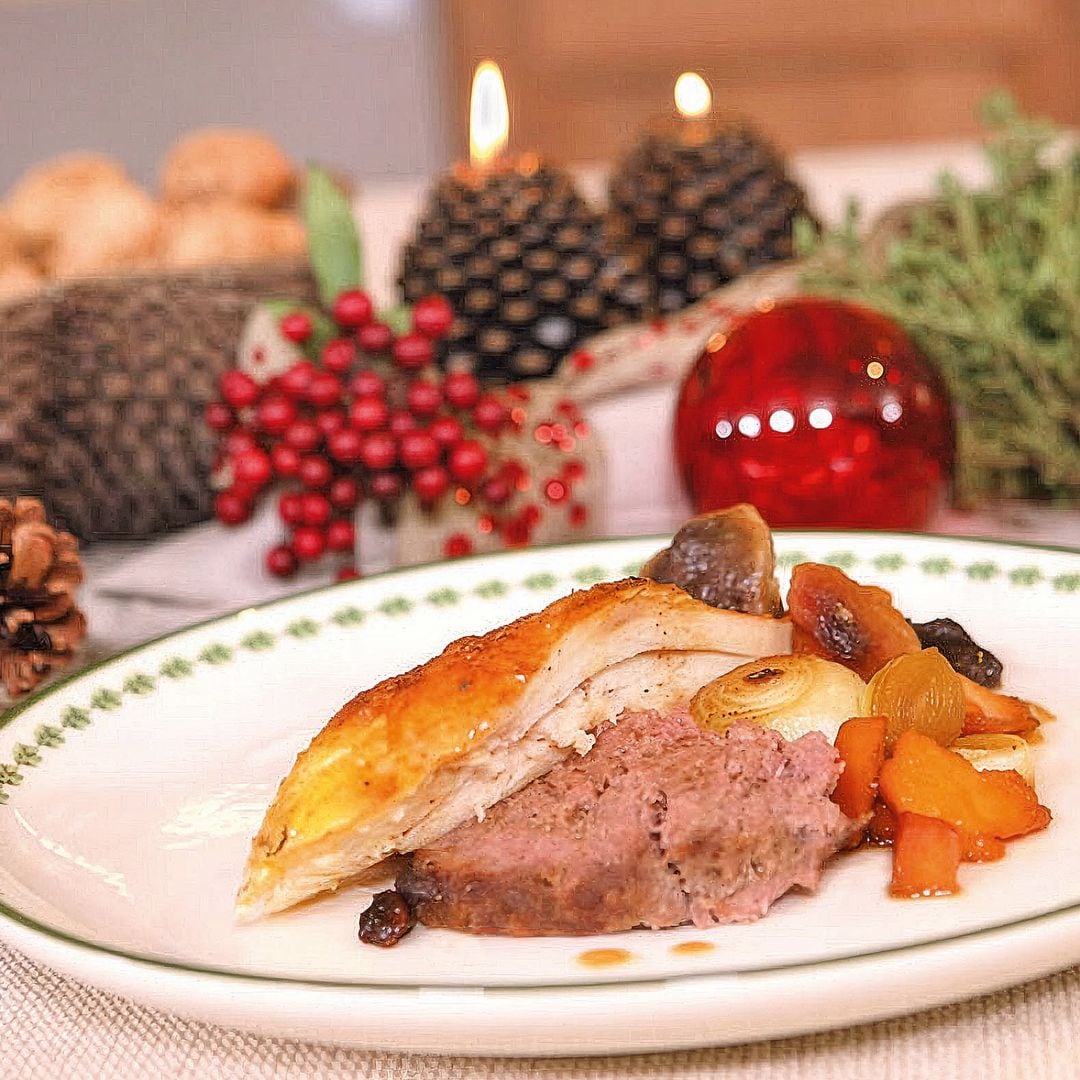 Plato de carne y vegetales en mesa decorada con velas y adornos navideños.