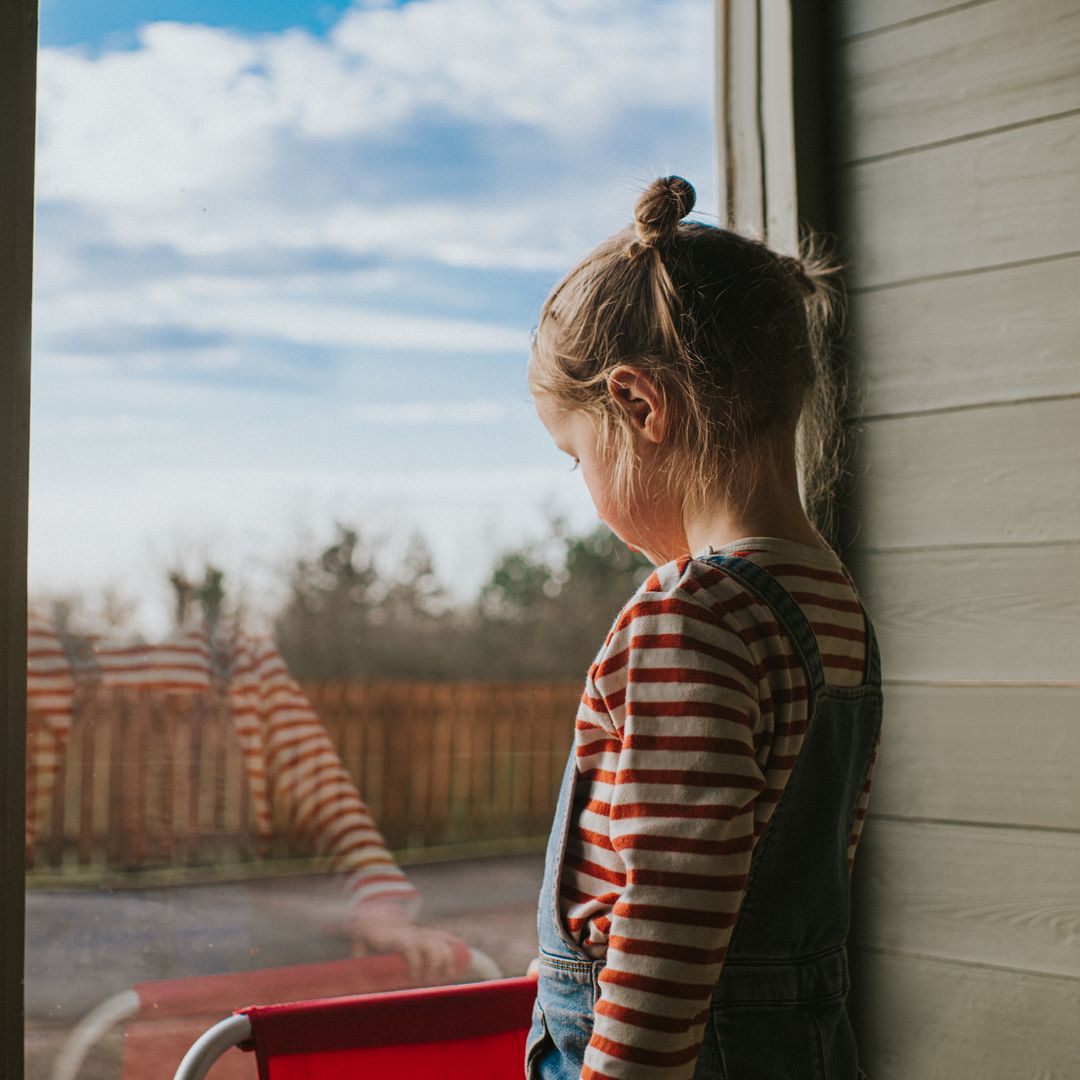 Niña triste junto a una puerta de cristal