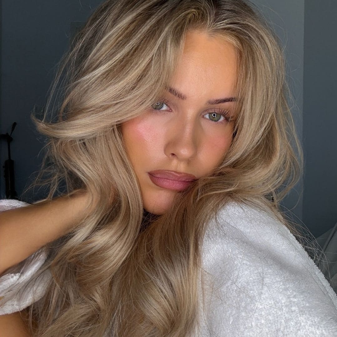 Aino Karolina con pelo rubio y ondulado con jersey blanco