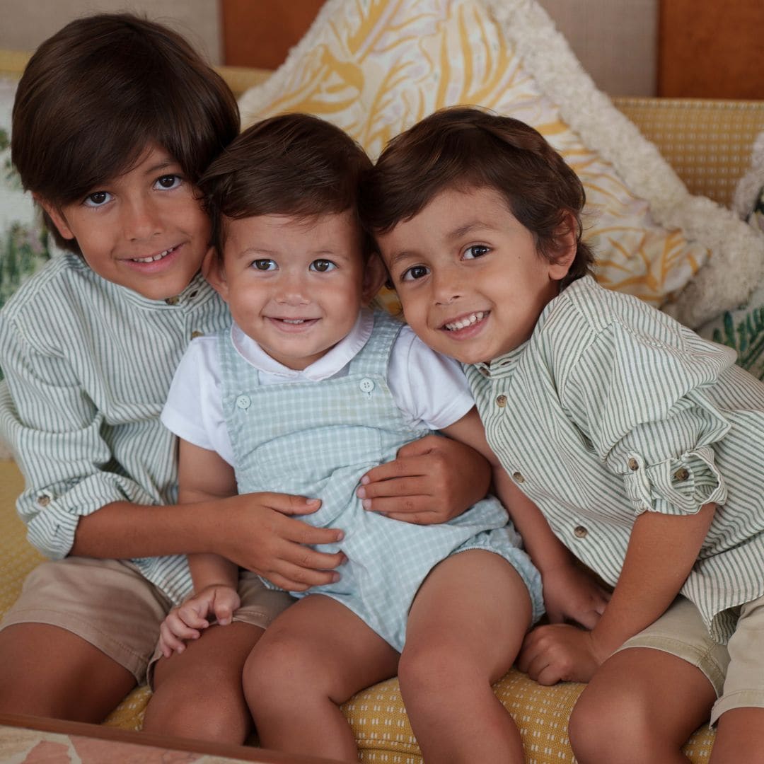 Miguel, Mateo y Martín sonrientes en un sofá, vestidos con ropa a rayas.