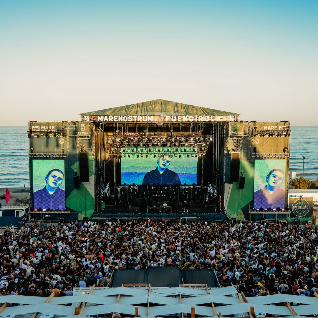 Gran multitud en un festival de música junto al mar, con un artista en el escenario.
