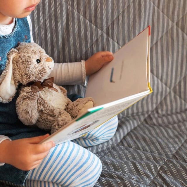 ni a leyendo un cuento con su osito de peluche en el sof 