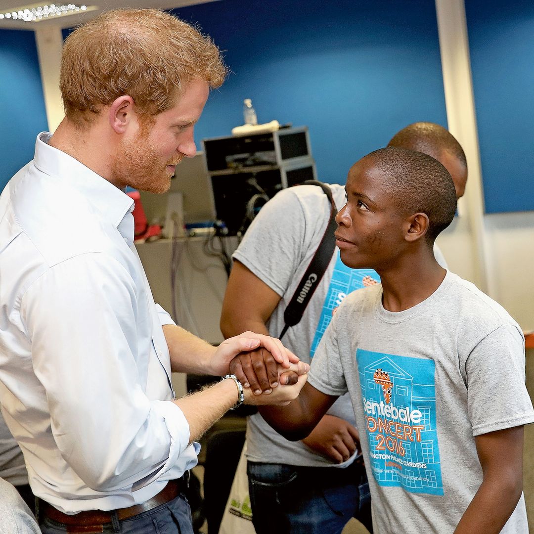El príncipe Harry cogiéndole la mano a un niño