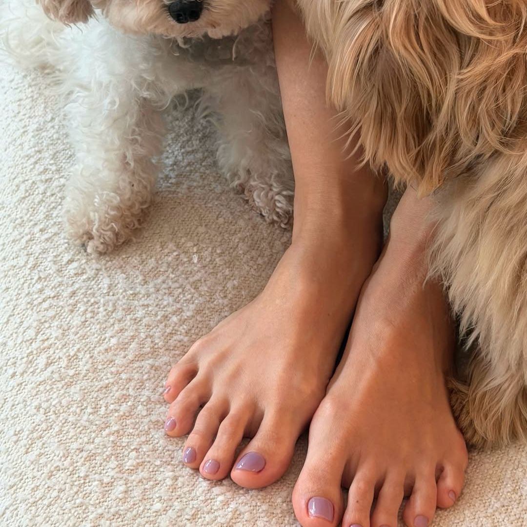 Pies de Tamara Falcó con pedicura malva y sus perros al lado