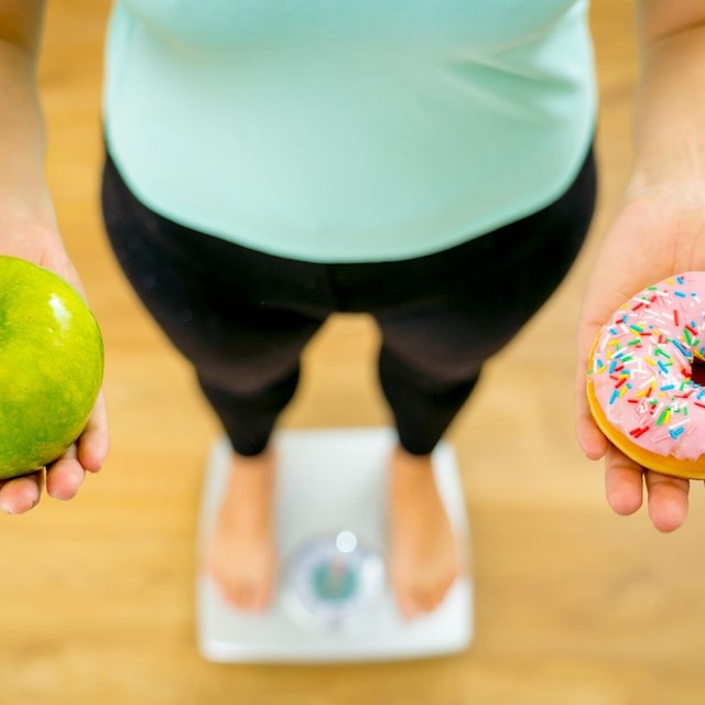 mujer sobre una b scula con una manzana en su mano derecha y una dona en la otra