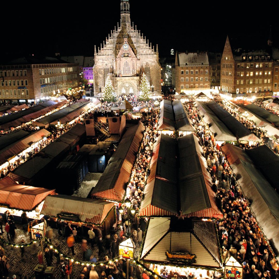 Vista aérea nocturna de un mercado navideño concurrido con personas y puestos festivos.
