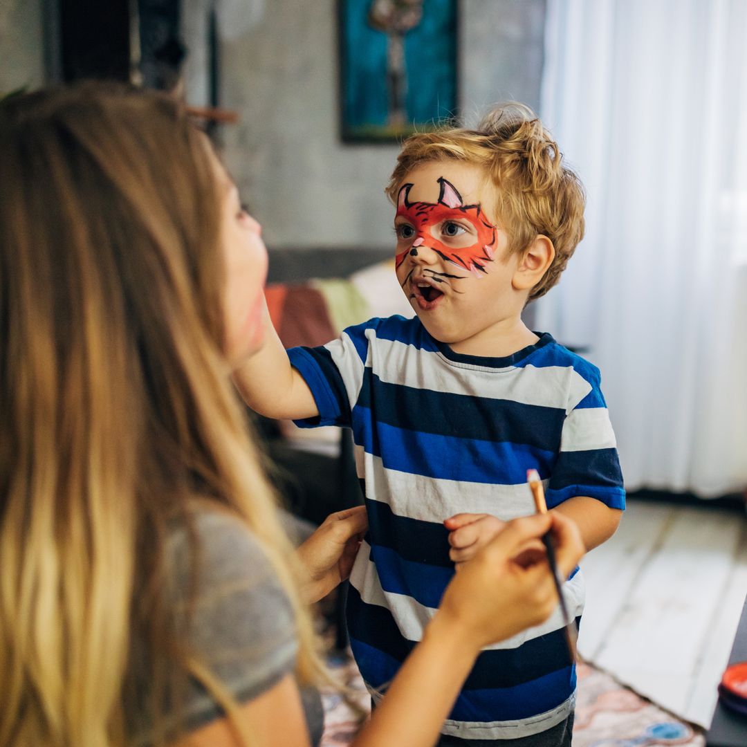 Madre maquillando a su hijo con una máscara de monstruo por Halloween