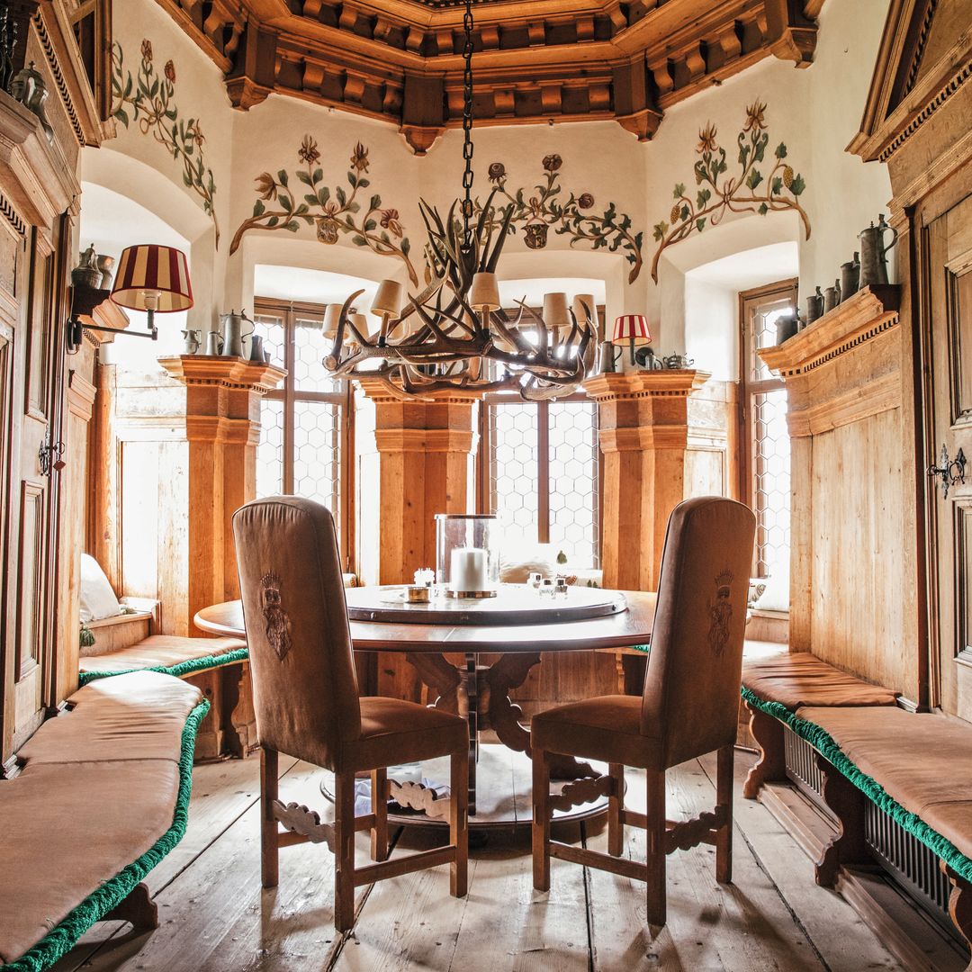 Sala de madera con mesa redonda y sillas, araña de luces, y bancos acolchados