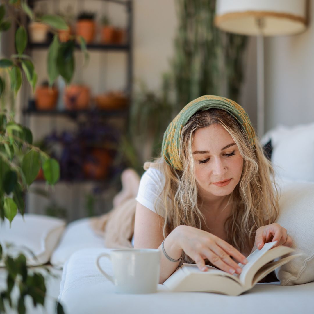 Chica joven leyendo relajadamente en el sofá de una zona exterior de su casa.