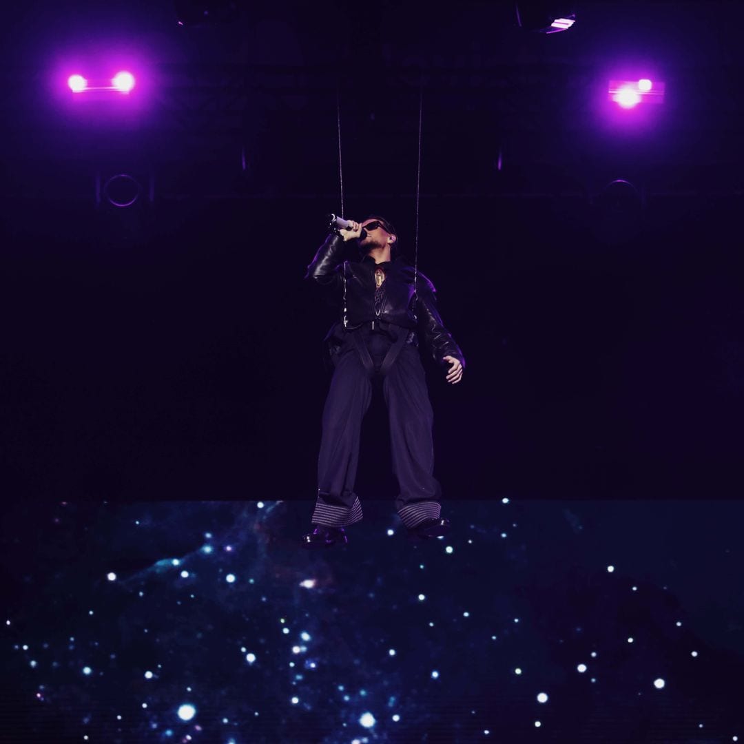 Abraham Mateo suspendido en el aire, cantando con micrófono en escenario con luces púrpura.