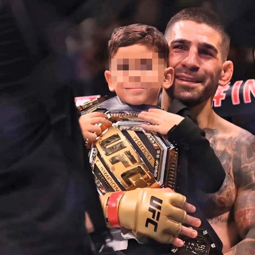 Ilia Topuria con tatuajes abraza a un niño con cinturón de campeón UFC.